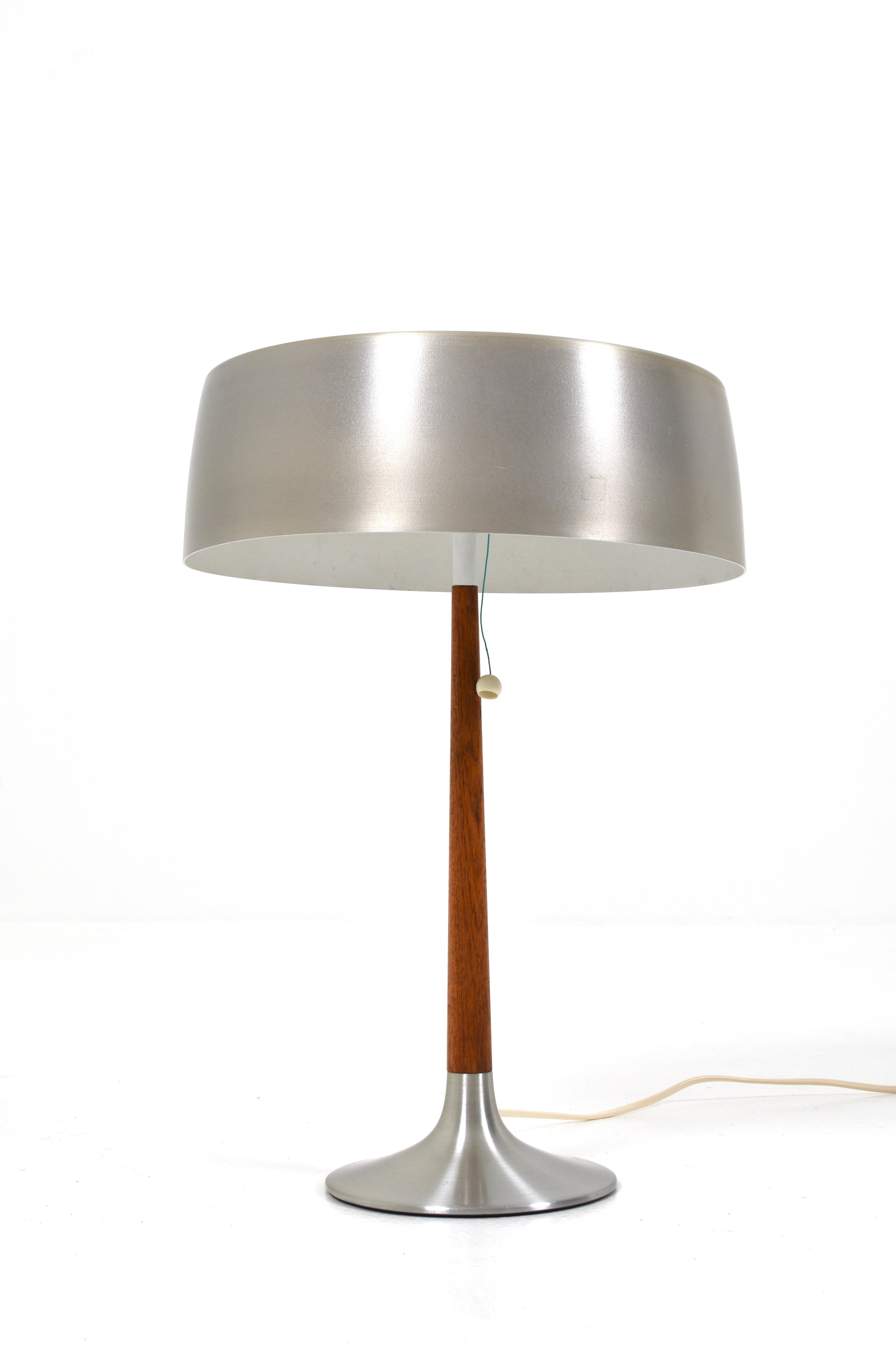 Die Lampe hat ein elegantes und stilvolles Design, das aus gebürstetem Aluminium und Teakholz besteht. Der Schirm der Lampe hat einige Gebrauchsspuren.