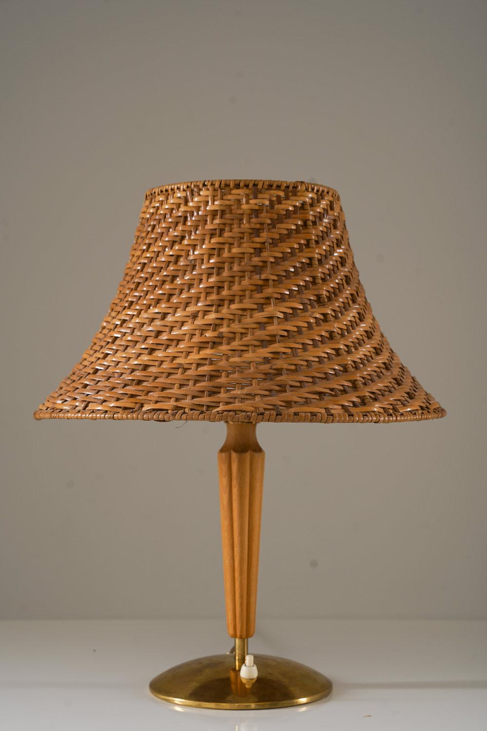 Swedish Modern table lamp in brass and oak, attributed to ASEA. This elegant lamp combines the natural warmth of an oak base with the sleekness of brass accents, creating a timeless Scandinavian look. The lamp is topped with a beautiful rattan