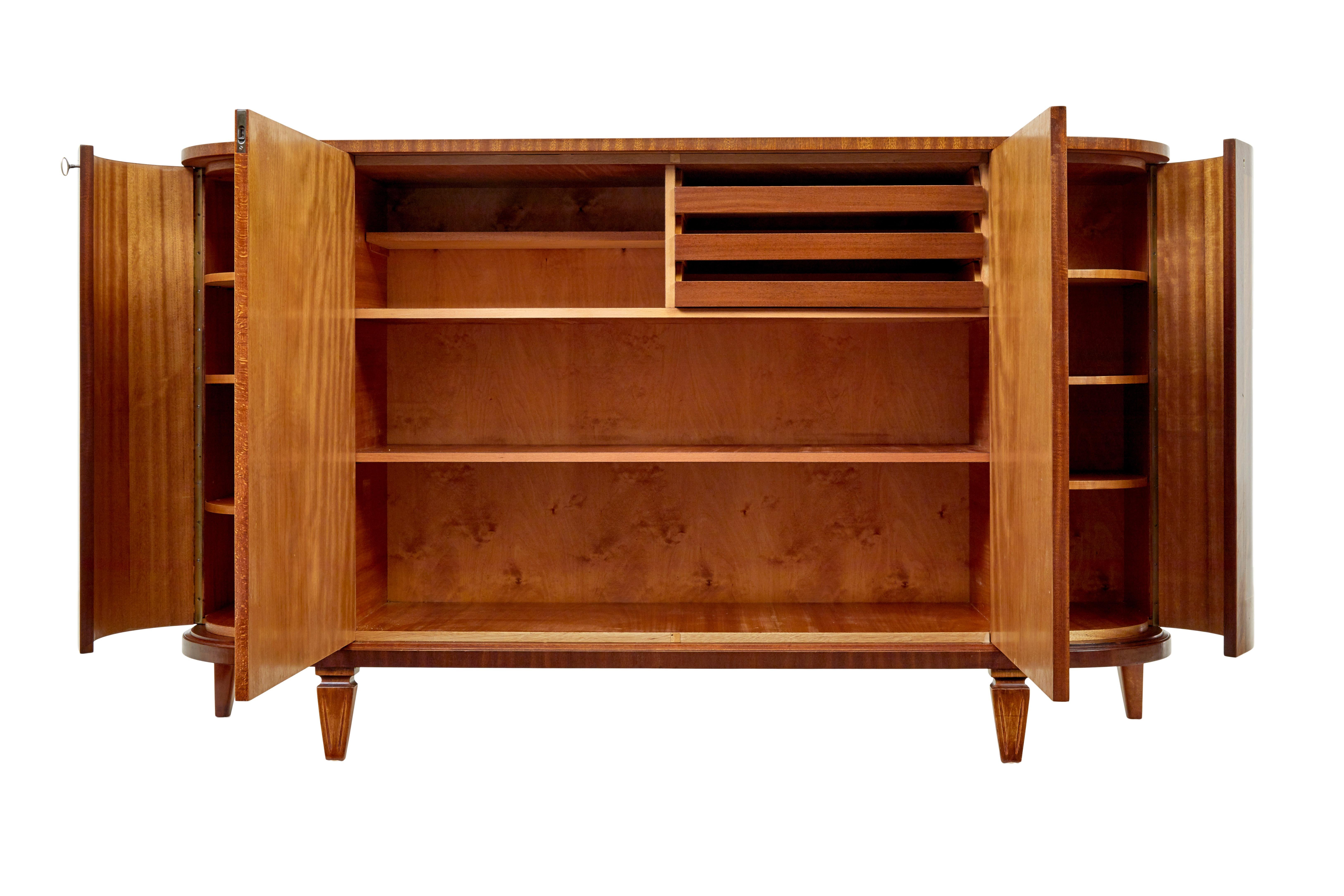 Credenza scandinava di metà secolo in teak intarsiato del 1950 circa.

Splendido buffet / credenza svedese della metà del secolo che utilizza impiallacciature e intarsi di mogano alla fiamma.

Pannello alto con piano sagomato, dotato di un armadio