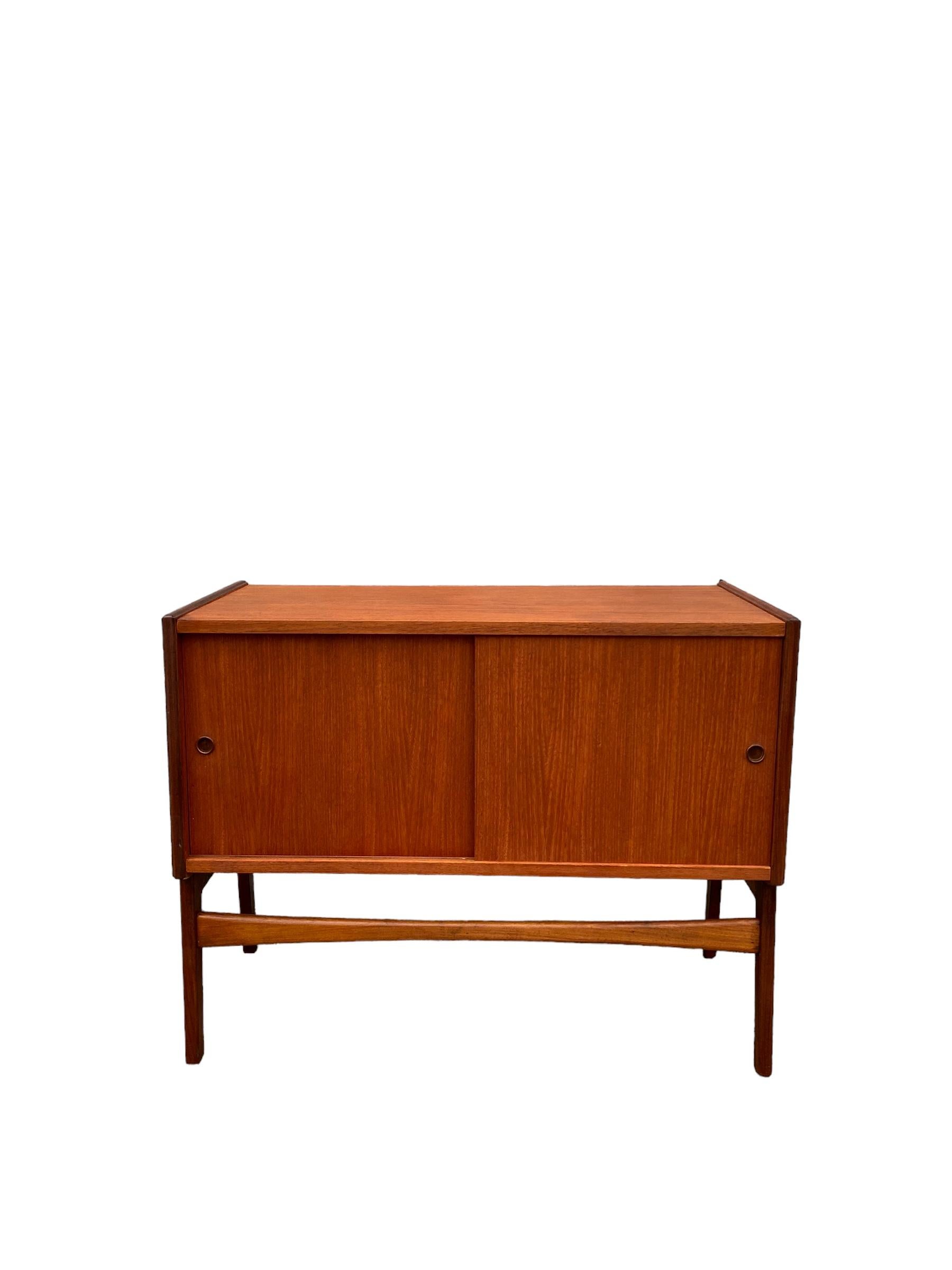 Handsome mid century petite teak record cabinet. Stamped Made in Norway. The cabinet features sculpted legs and bow tie stretchers with two sliding doors. Good even grain throughout.