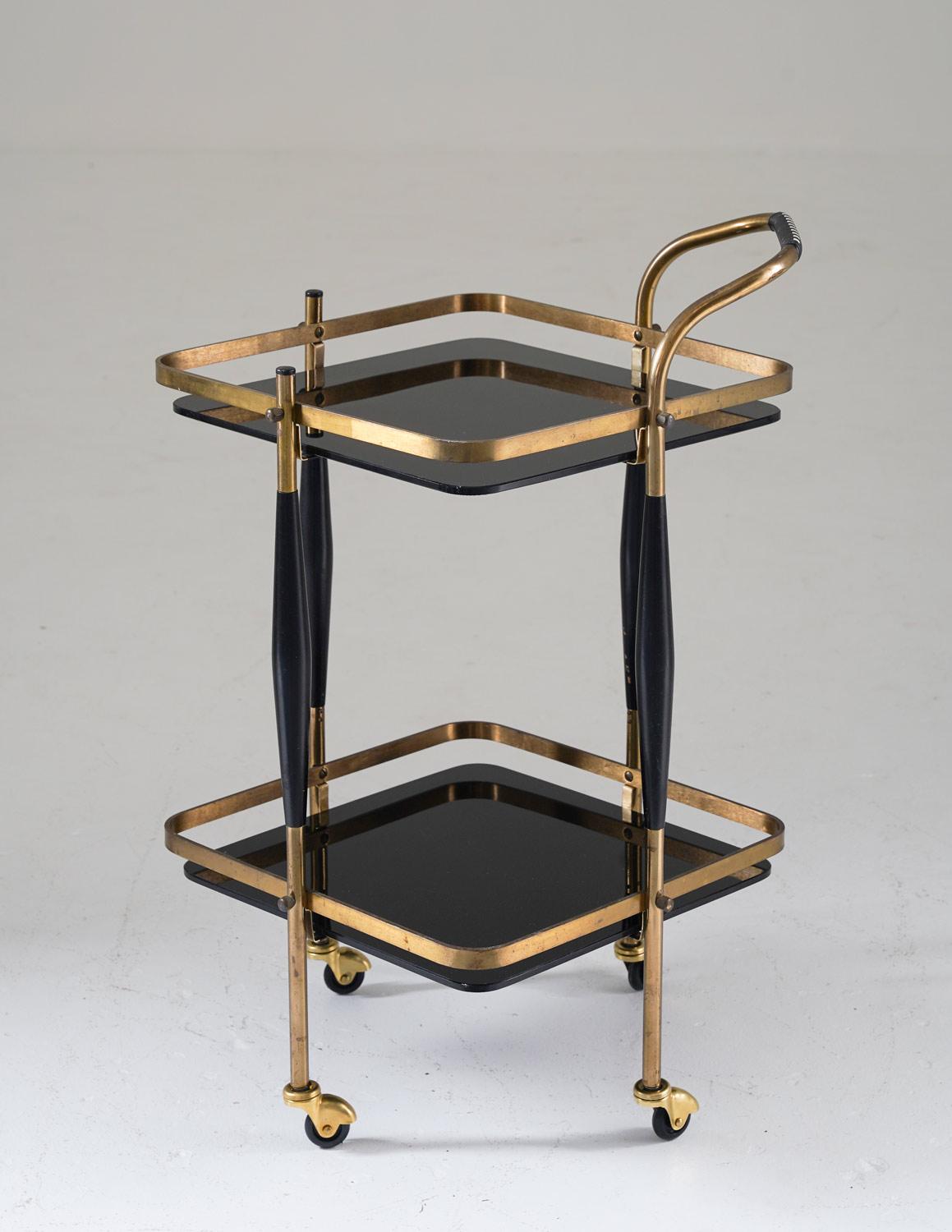 A beautiful bar cart made of brass with black wooden details and a table top in glass, probably produced in Sweden. 
Beautiful design and well matched materials make this piece a good fit in a modern home. It consists of a frame in brass and wood