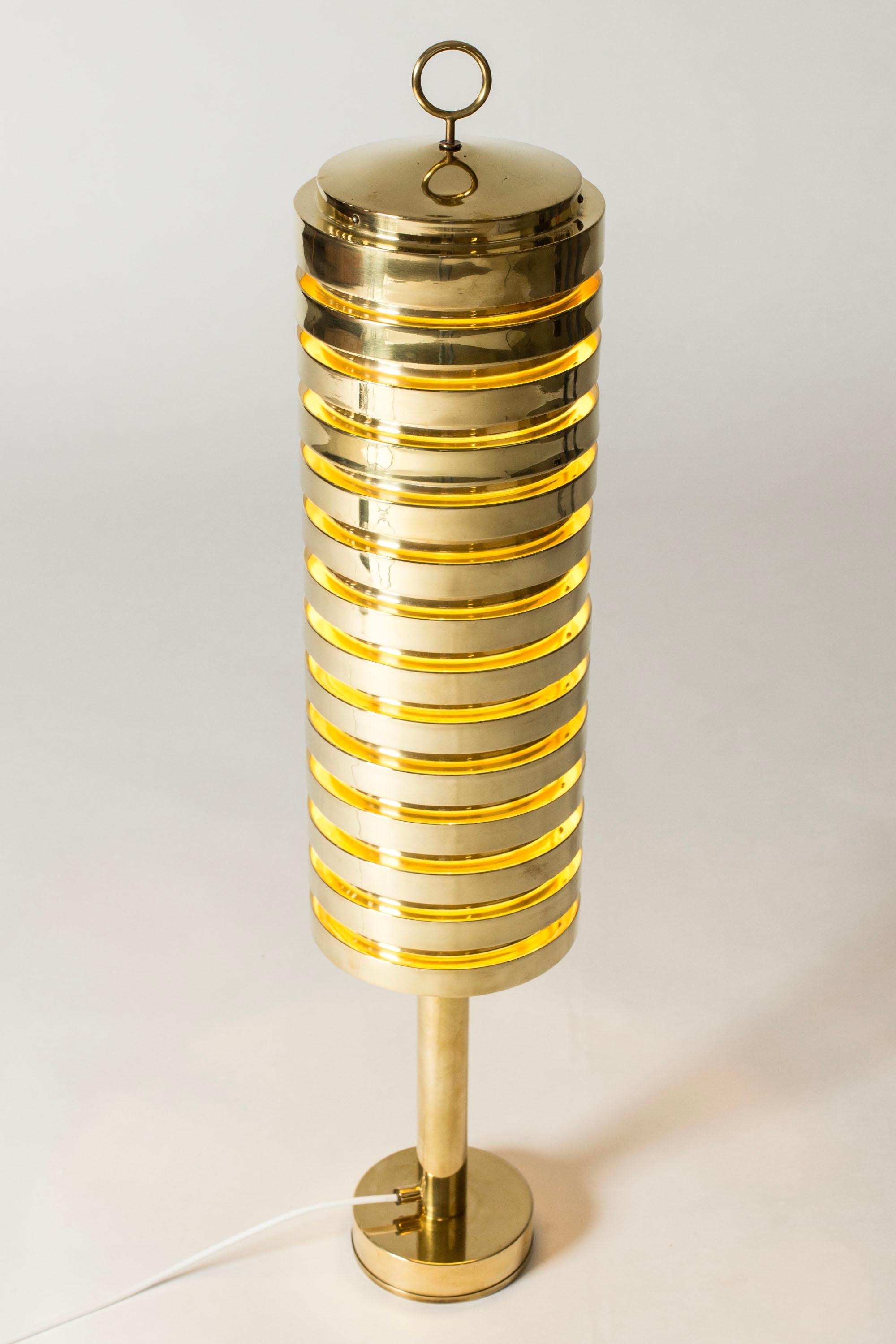 Rare, striking brass floor lamp by Hans-Agne Jakobsson, model #G-81. Tall cylinder form with a decorative hoop on top. Brass lamellas are stacked in a tight design letting the light out with a warm glow.