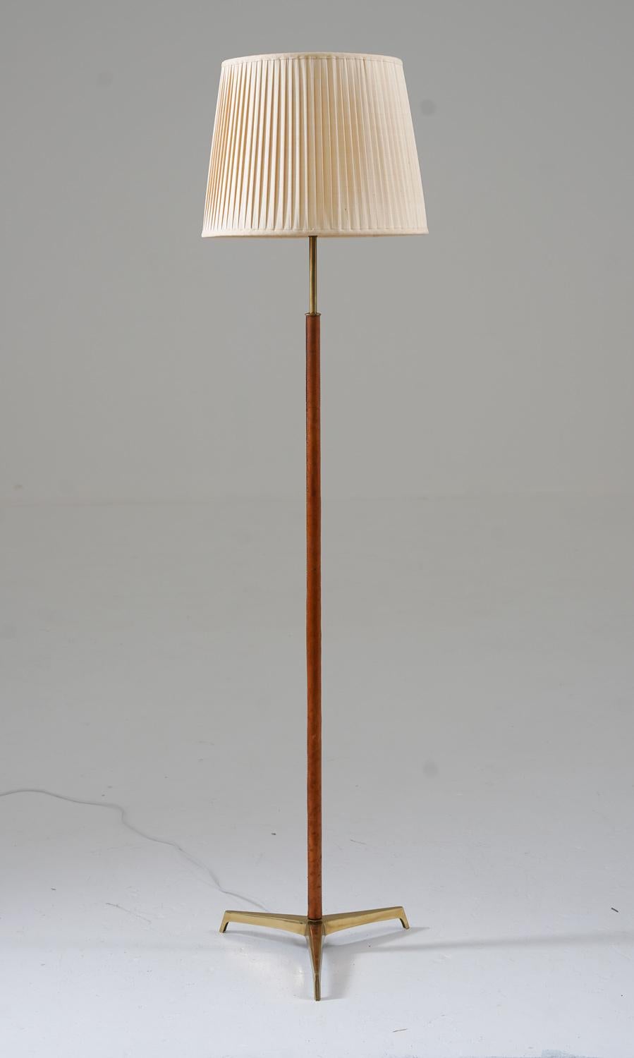 Scandinavian midcentury tripod floor lamp in brass and leather, manufactured in Sweden, 1960s.
This lamp consists of a leather-covered brass base, resting on a tripod foot in solid brass. The lamp comes with a beautiful vintage shade.