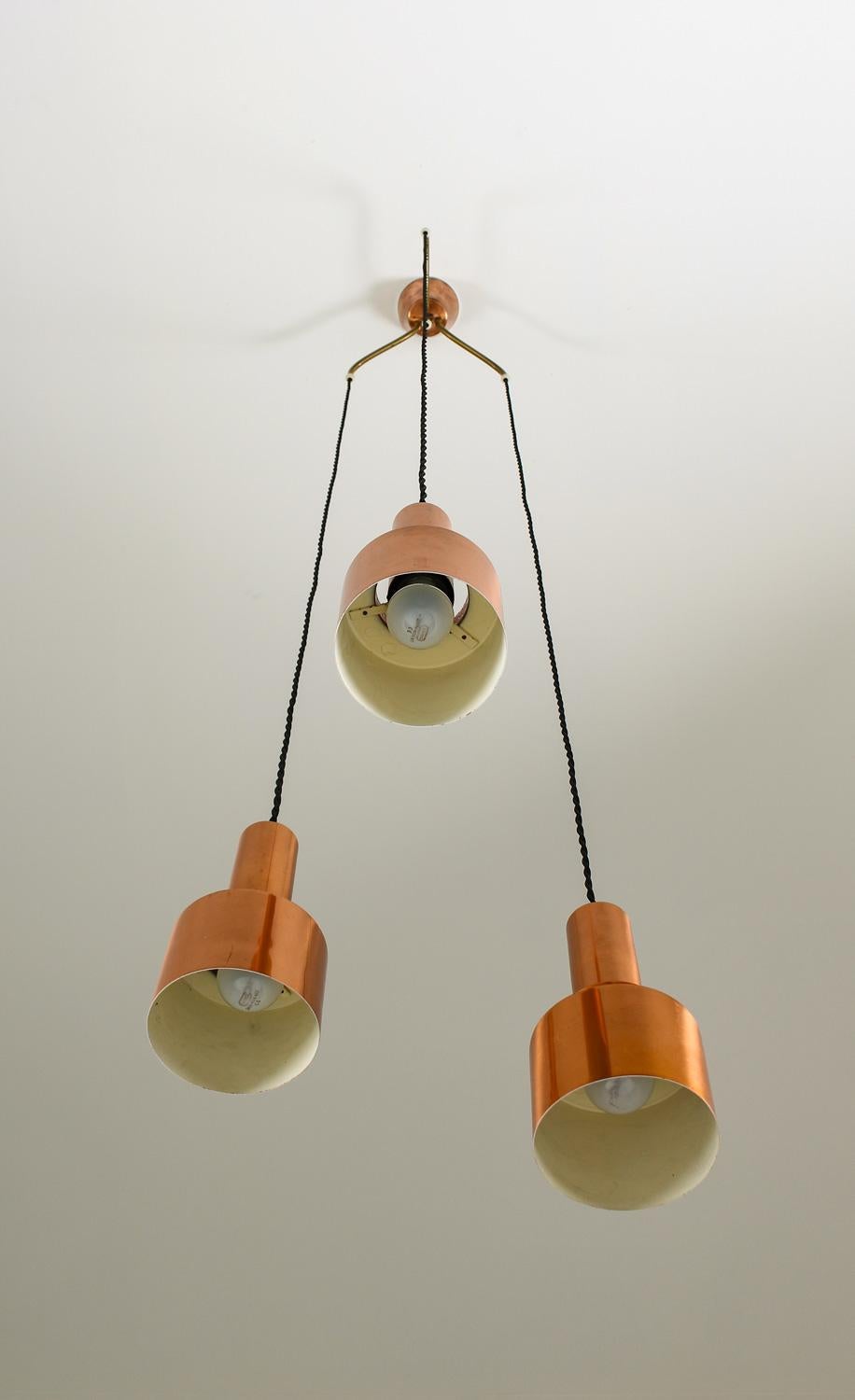 Wonderful early pendants, model T292, in solid copper by Hans-Agne Jakobsson, designed 1958. 
The lamp consists of three pendants connected by a divider in copper and brass. The light spreads beautifully from the perforated copper