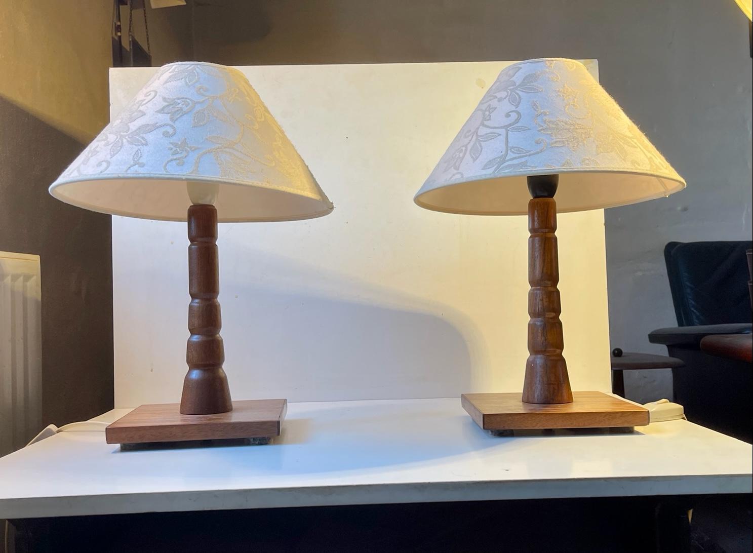 A set of teak table lamps turned with stepped architectural details to their stems. Manufactured in Scandinavia, probably Sweden, during the late 1960s. They are mounted with vintage textile shades with floral impressions and has on/of switches to