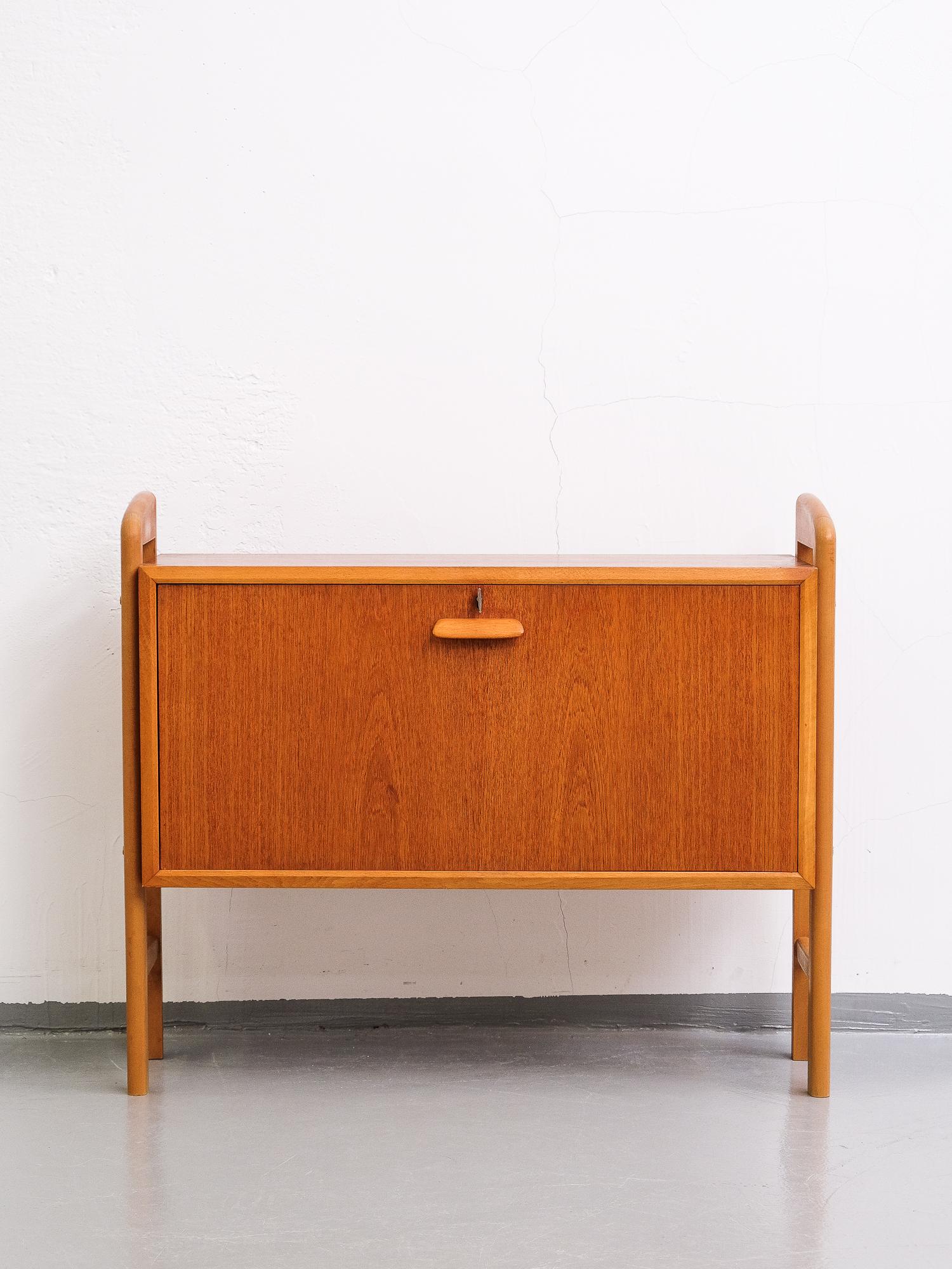 Nice little Scandinavian teak bar cabinet. A drop-down front opens onto a roomy interior with shelf, two little drawers, a mirrored back and a light.