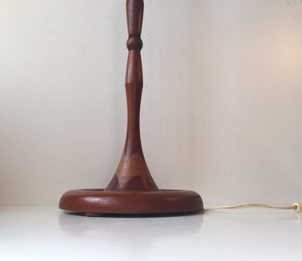 A Scandinavian floor lamp composed of teak joints separated by brass ring. It features cherrywood intarsia to its organically shaped base and an on/of switch beneath the shade. It was manufactured in Denmark or Sweden during the 1960s by an