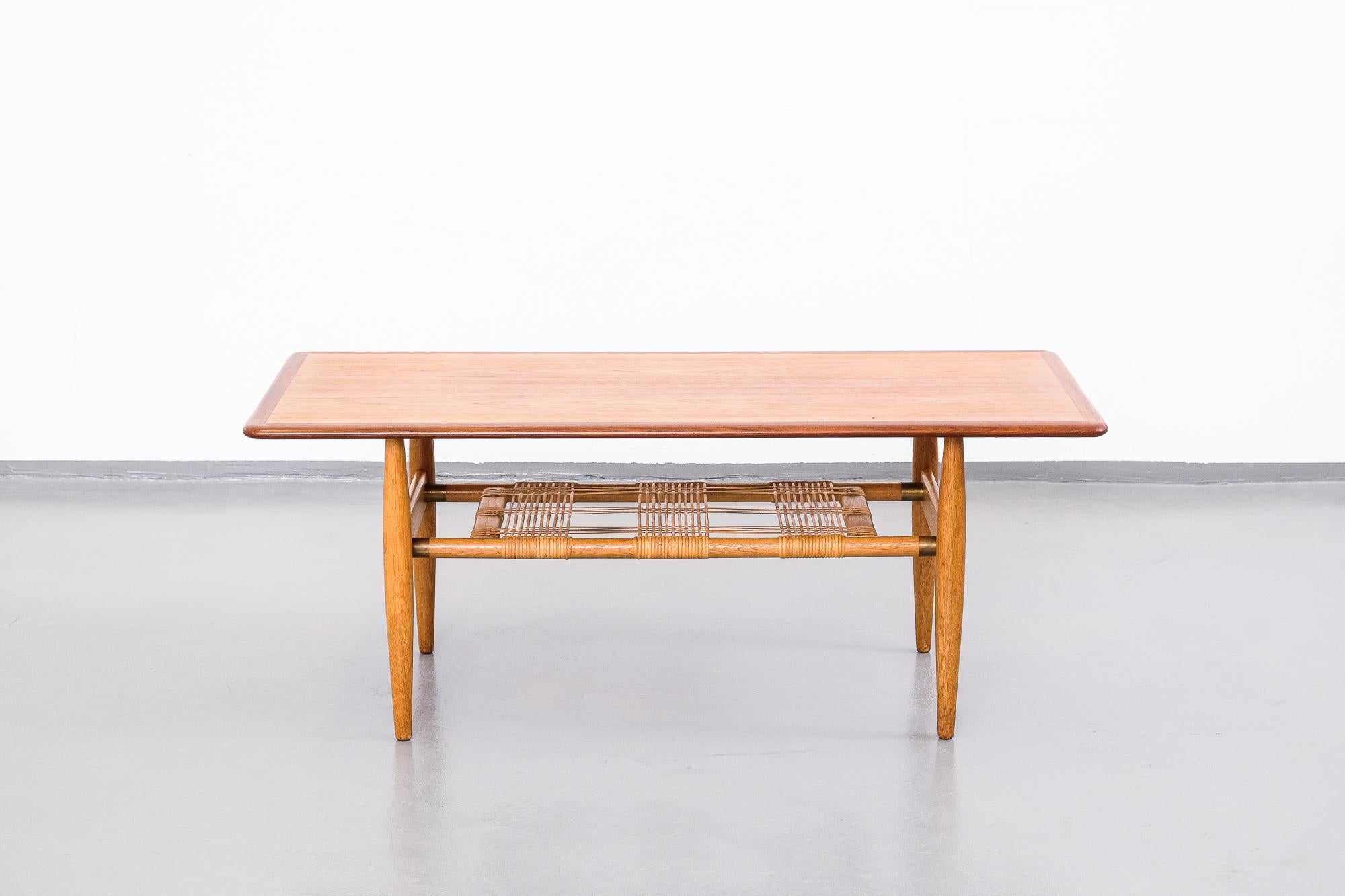 Great Scandinavian midcentury coffee table, probably Danish but unknown designer. Teak top, oak frame and woven cane shelf with brass details.