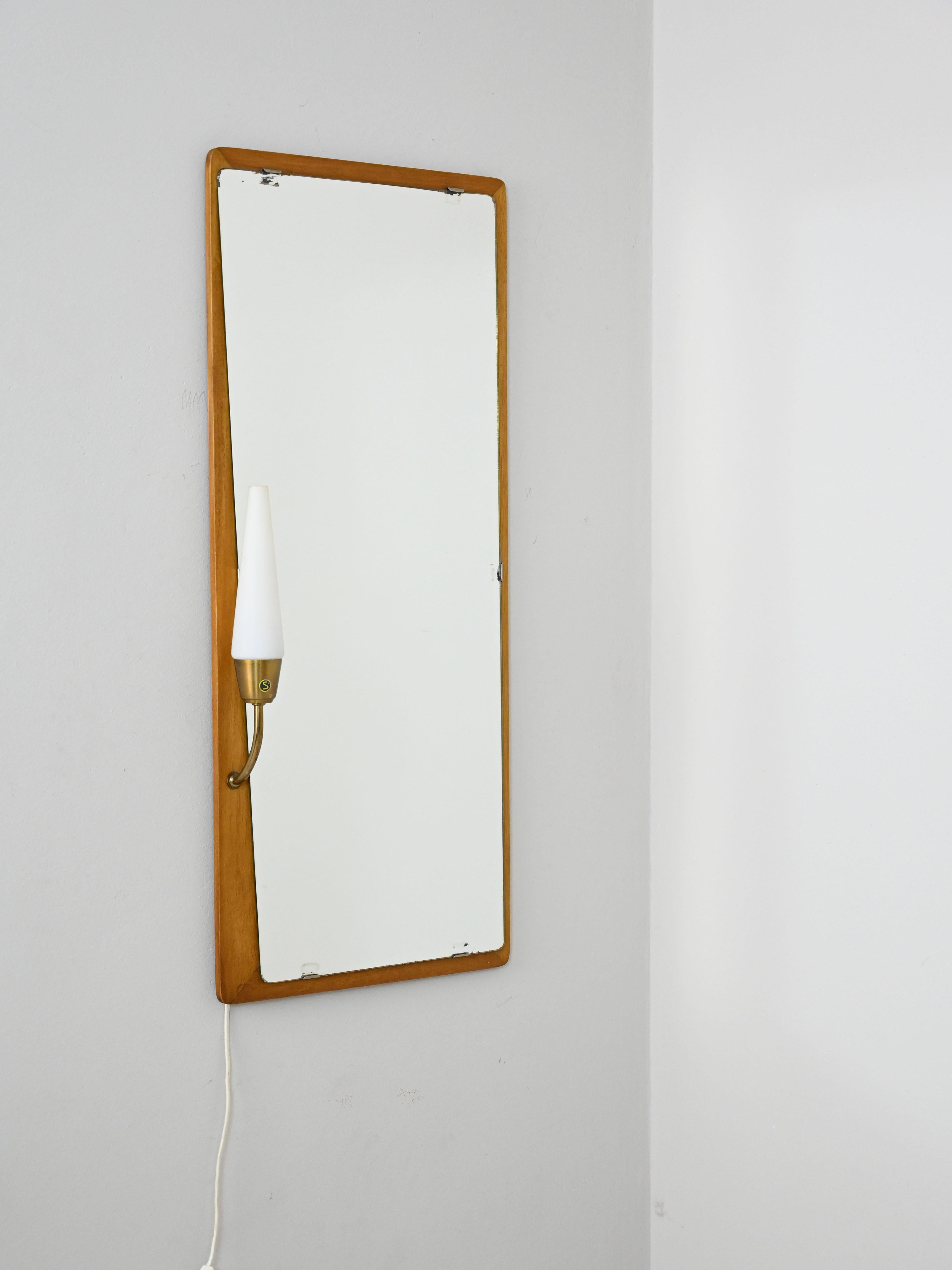 Vintage 1960s mirror equipped with lighting.

An original complement with classic lines typical of the period.
The teak frame has a light point consisting of a gilded metal stand and an opaline glass shade.
Perfect as an entryway or bathroom