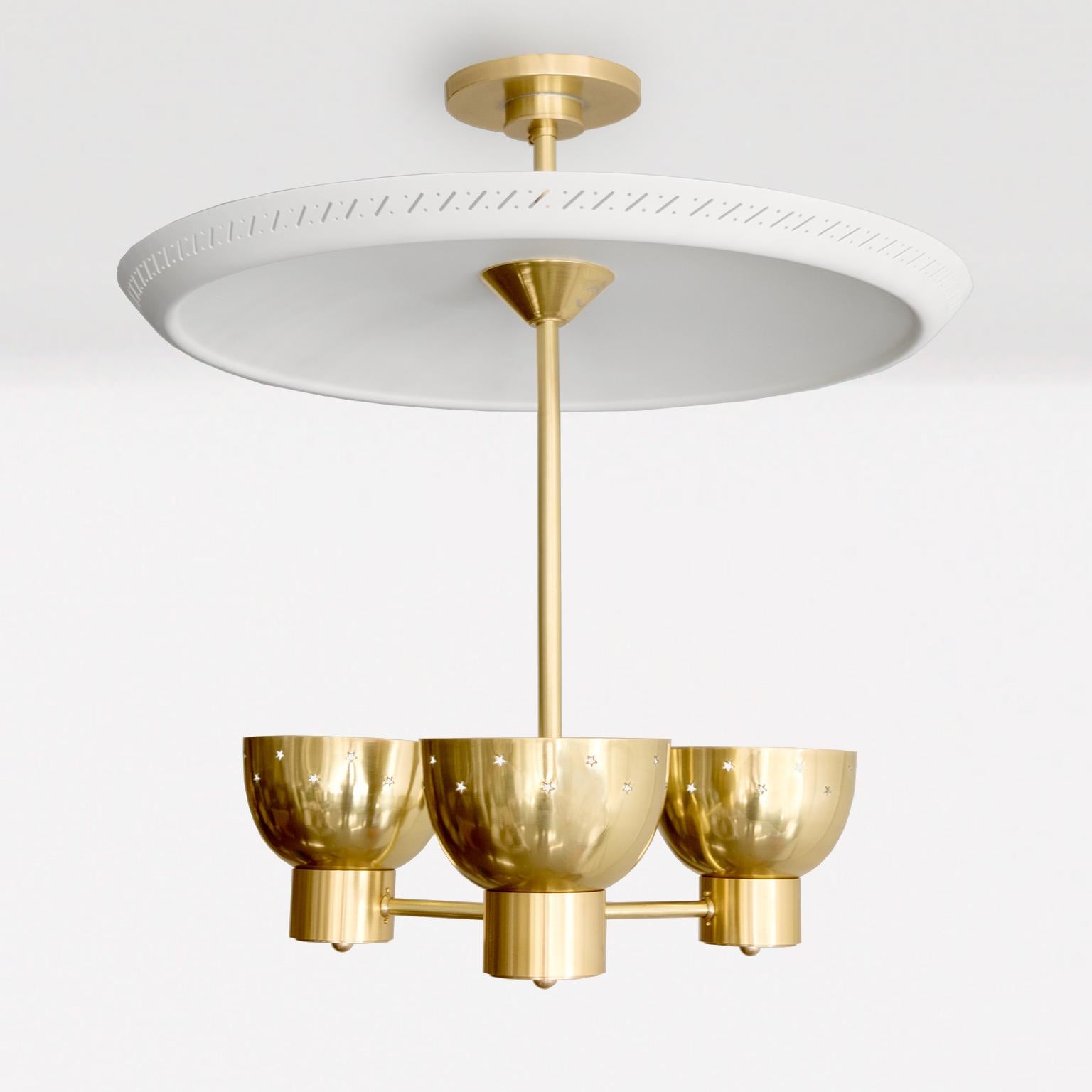 Lampadario a 3 paralumi in ottone con grande riflettore in vernice bianca laccata. Il rivestimento del riflettore è caratterizzato da una fascia di capsule e ritagli a forma di cerchio. I 3 paralumi in ottone lucido contengono ciascuno una presa a
