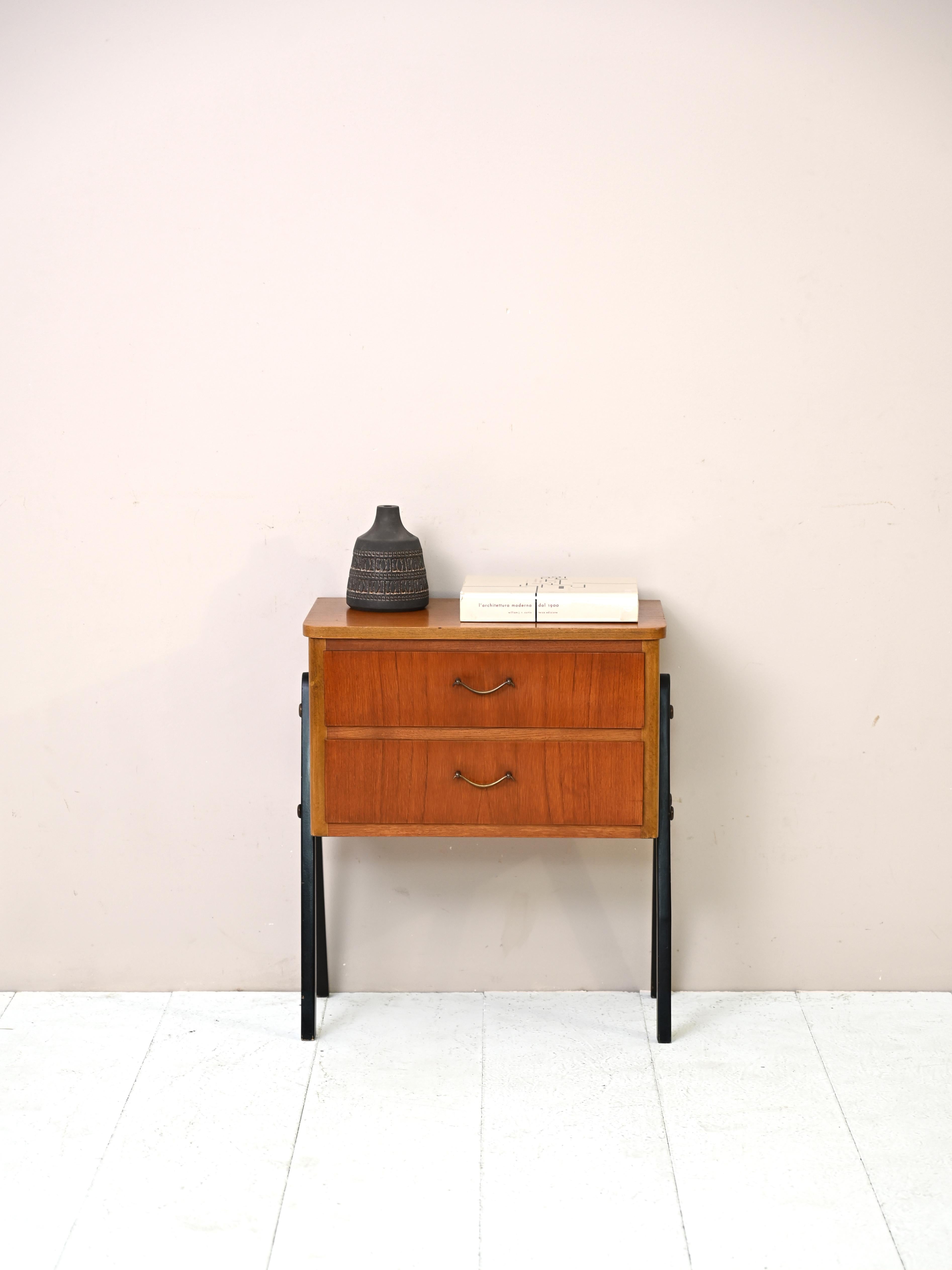 Small teak wood chest of drawers with typical mid-century Scandinavian shapes.

The stem consists of two drawers that are supported by the long wooden legs painted black.

This elegant bedside table is perfect for giving a Northern European