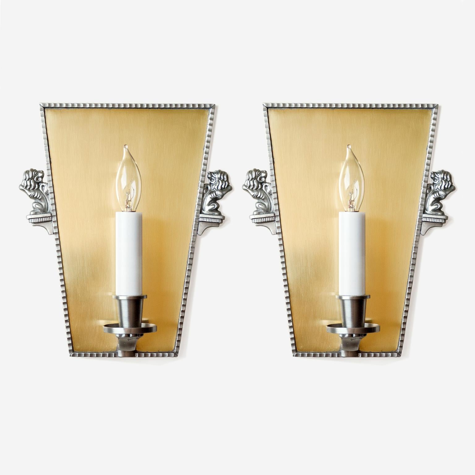 Scandinavian Modern keystone shaped pair of Swedish Art Deco wall sconces in polished brass with pewter details. The sconces each have a single candle with candelabra socket, a pewter detail frames the brass backplate and pewter opposing lions flank