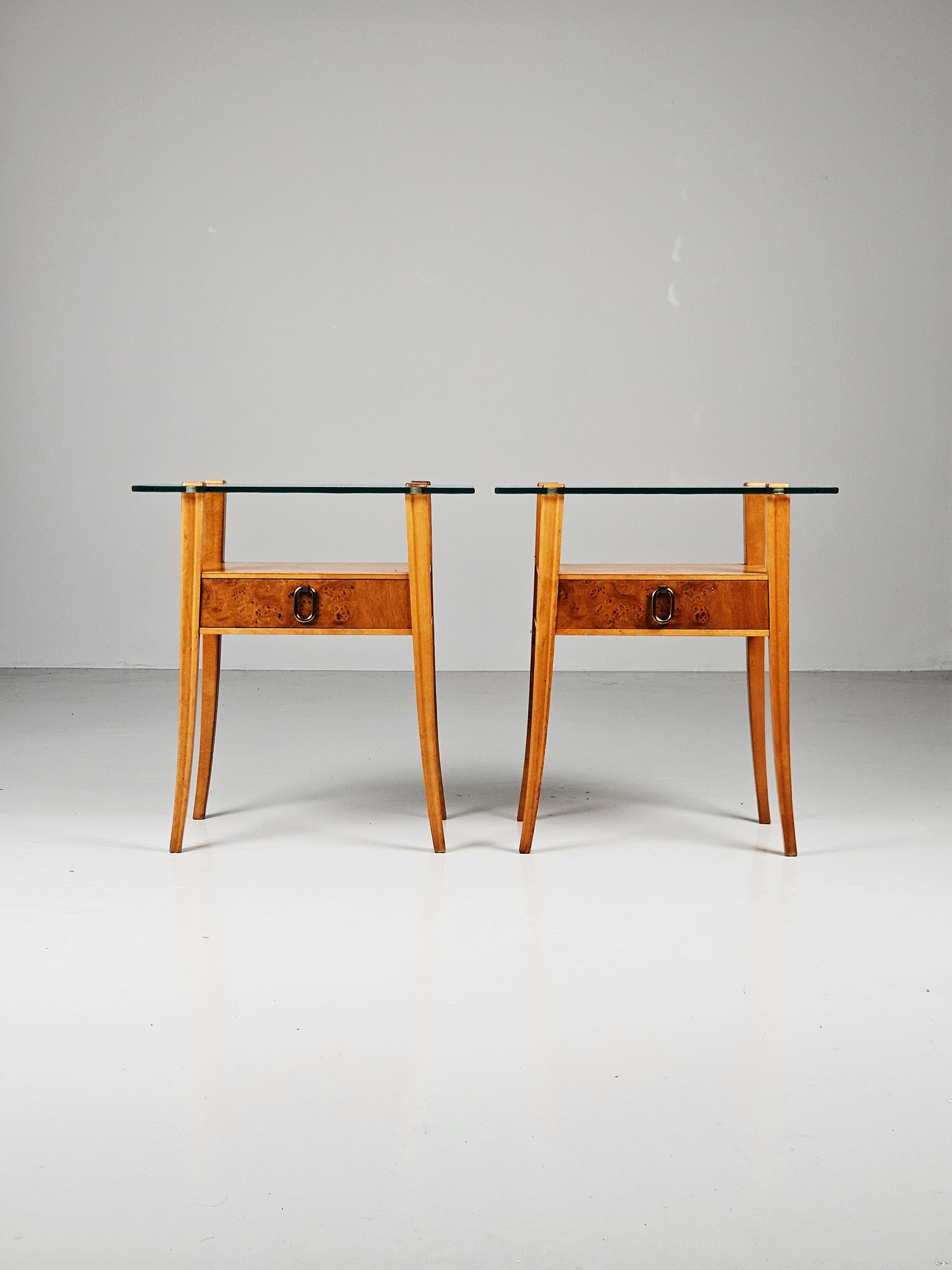 Magnifique paire de tables de chevet produite par Svenska Möbelfabrikerna Bodafors, Suède, au cours des années 1950. 

Fabriqué en bouleau avec un placage de racines sur les tiroirs et une poignée en laiton. Magnifique plateau en verre. 

Design
