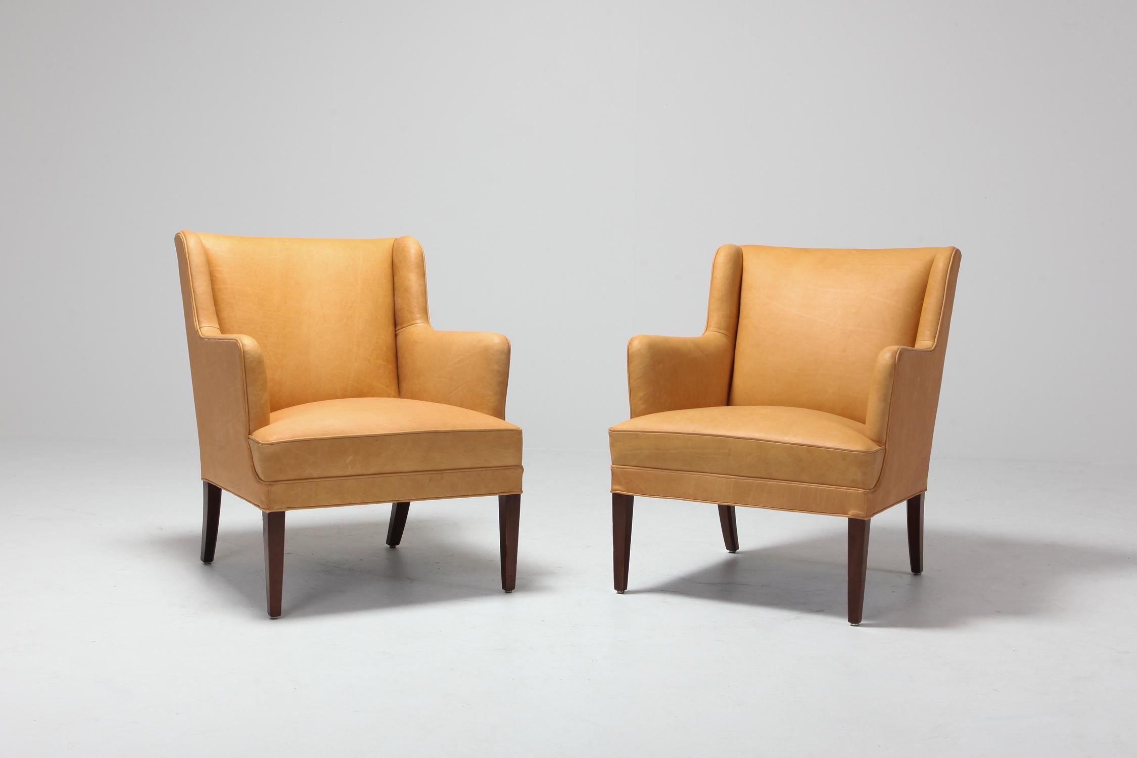 Mid-Century Modern armchairs in camel colored leather 
Reminds a bit of the designs of Nanna Ditzel and Arne Norell.

 