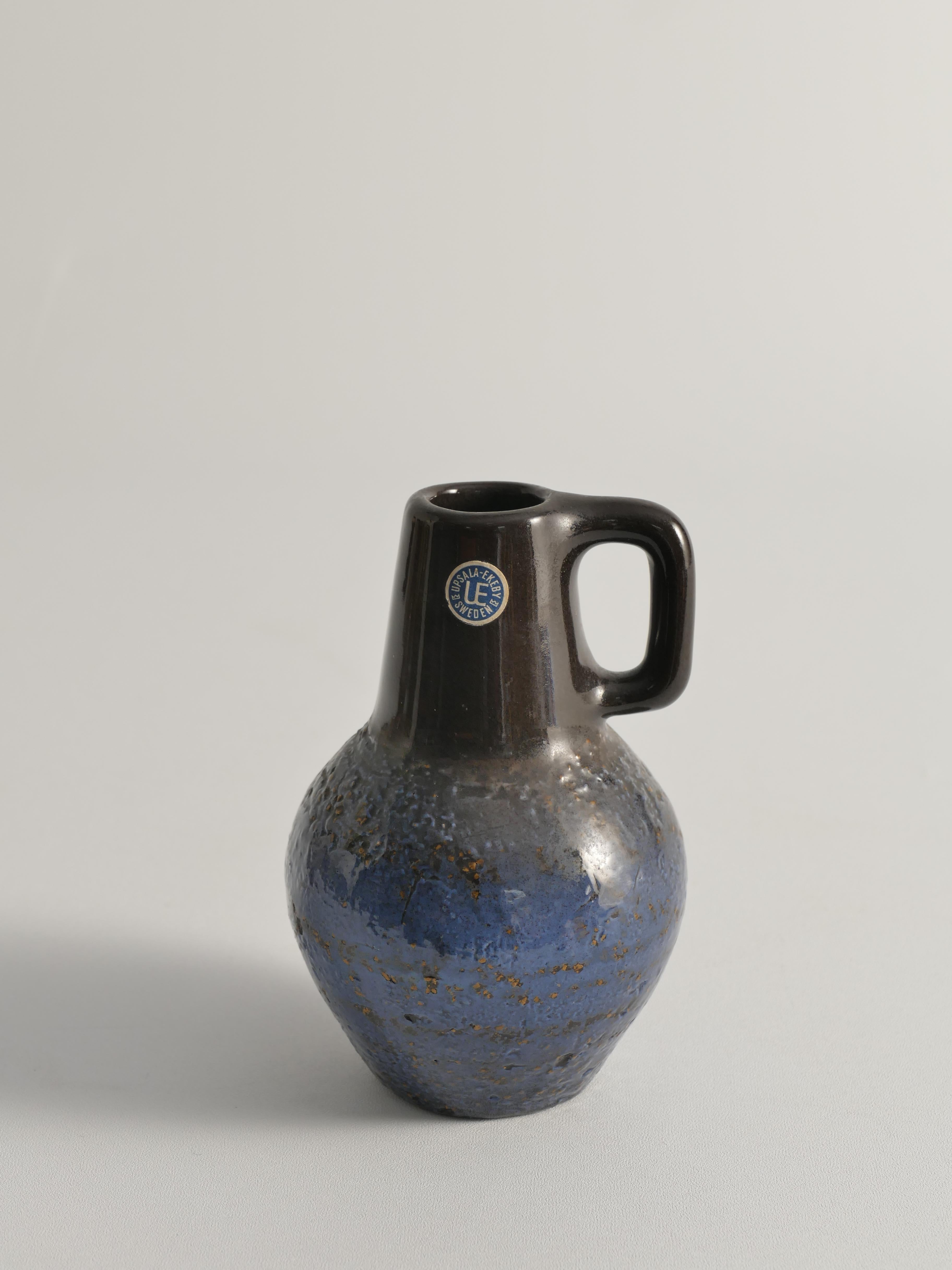 Realizzato dalla rinomata ceramista Ingrid Atterberg per Uppsala Ekeby, questo vaso in chamotte nera e blu con un manico distintivo e una superficie ruvida incarna il design moderno scandinavo di metà secolo. Progettato esclusivamente come parte
