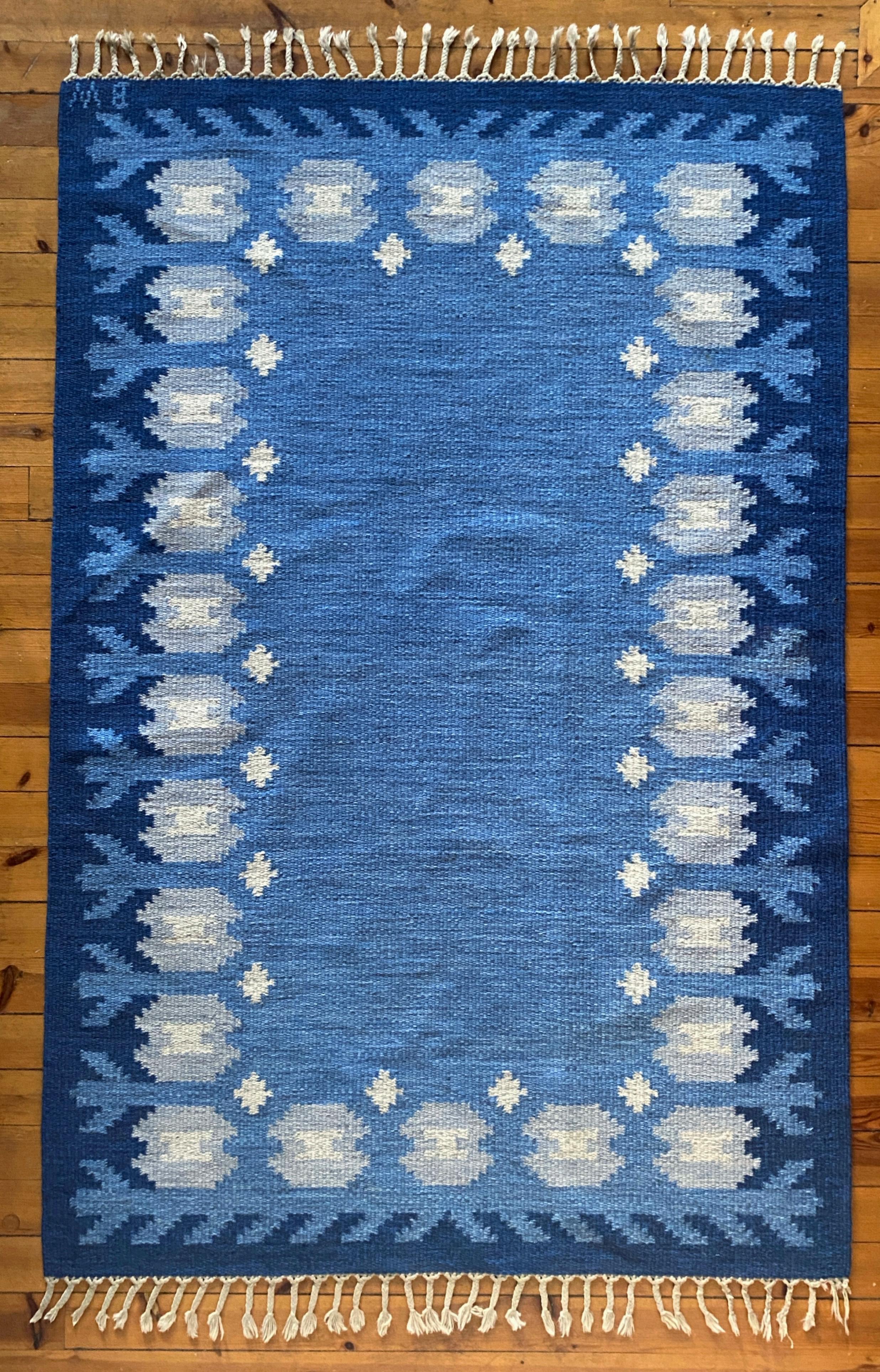 Tappeto moderno scandinavo a tessitura piatta in rölakan blu dell'artista tessile svedese Berit Koenig Woelfer, anni '60. Questo tappeto in lana fatto a mano su un ordito di lino presenta fiori stilizzati di colore blu chiaro su un centro blu medio,
