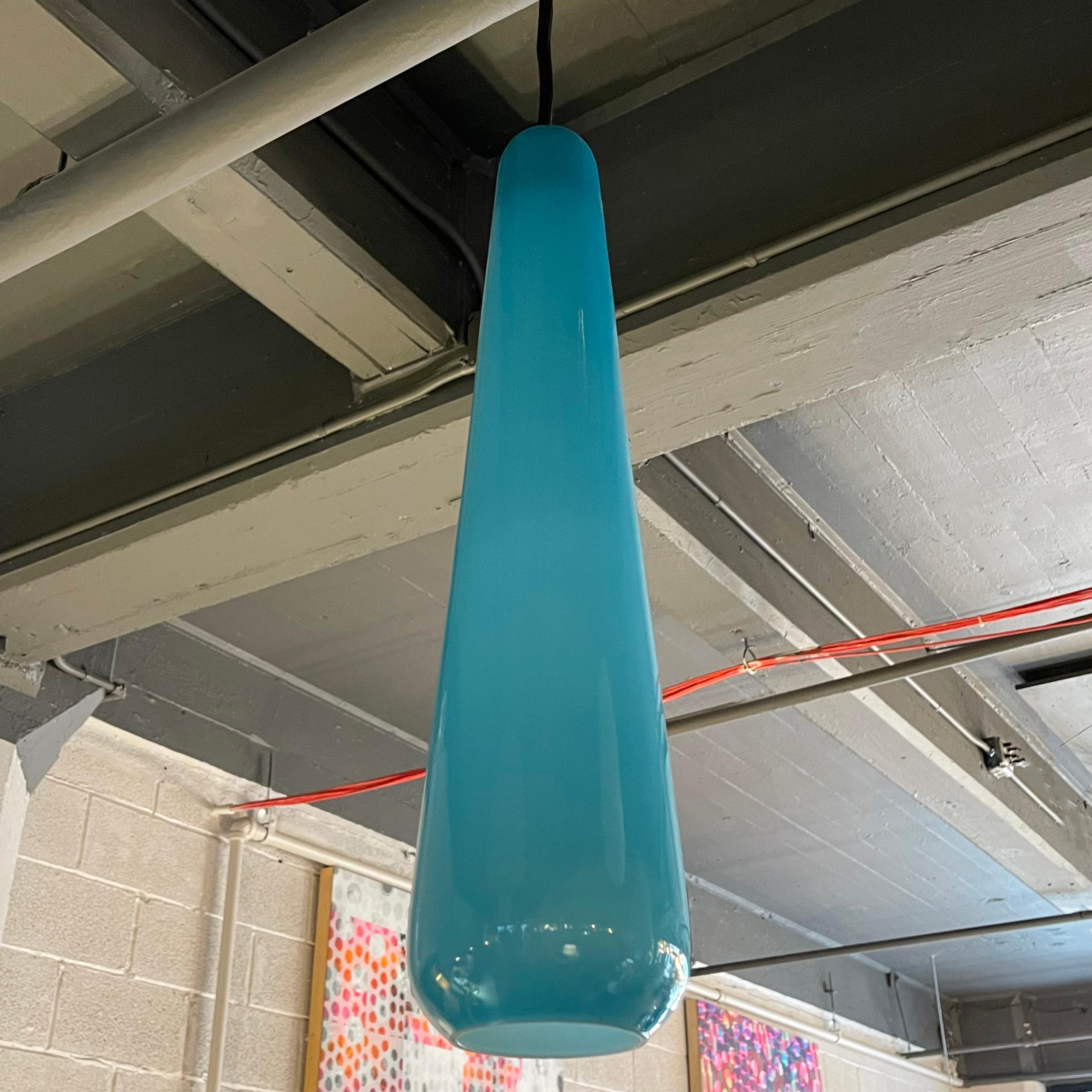 Scandinavian modern, art glass pendant light features an elongated, light blue teardrop shade with white interior on black cord with brass disc canopy. The pendant is newly wired to accept up to a 75 watt medium socket bulb and hangs at an overall
