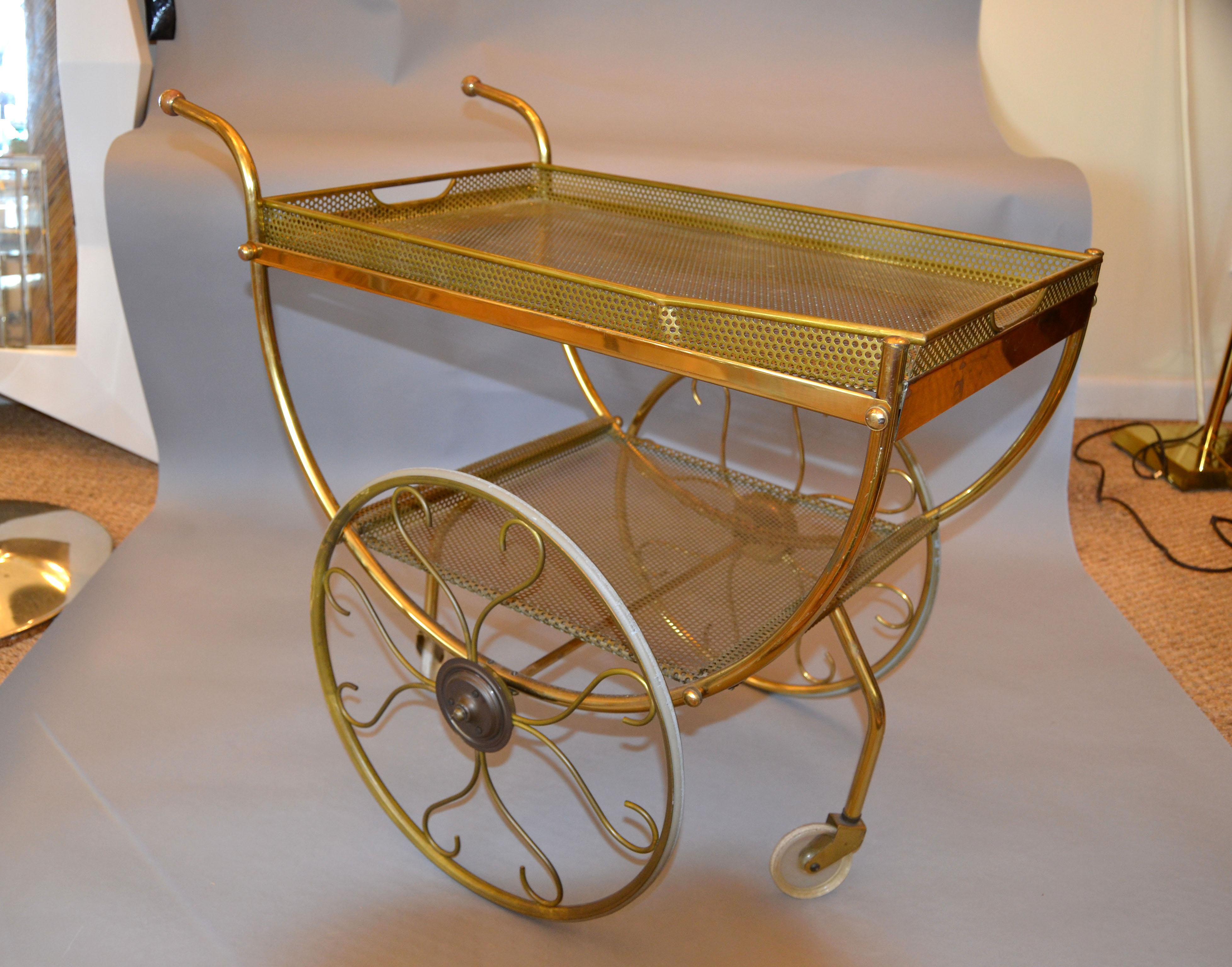 Chic 1950s Scandinavian modern brass bar cart designed by Josef Frank and manufactured for Svenskt Tenn in Sweden.
Made out of tubular and perforated brass. Wire mesh brass tray on top and at the bottom a shelf. The 2 smaller wheels are made out of