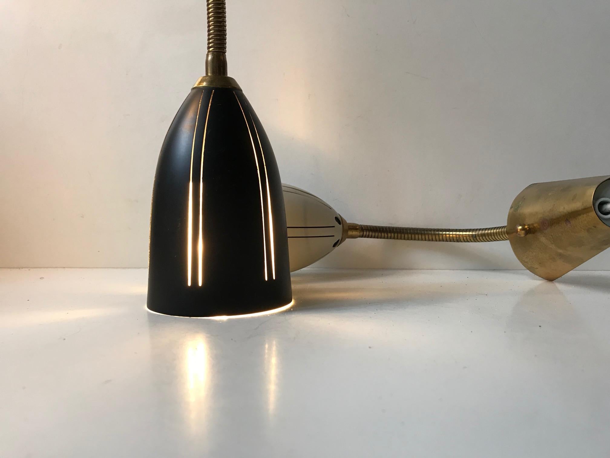 A set of flexible and adjustable wall lamps in brass with perforated aluminium shades. One is white and one is black with slight differences in dimensions and design features. They were manufactured and designed by EWÅ in Sweden in a style