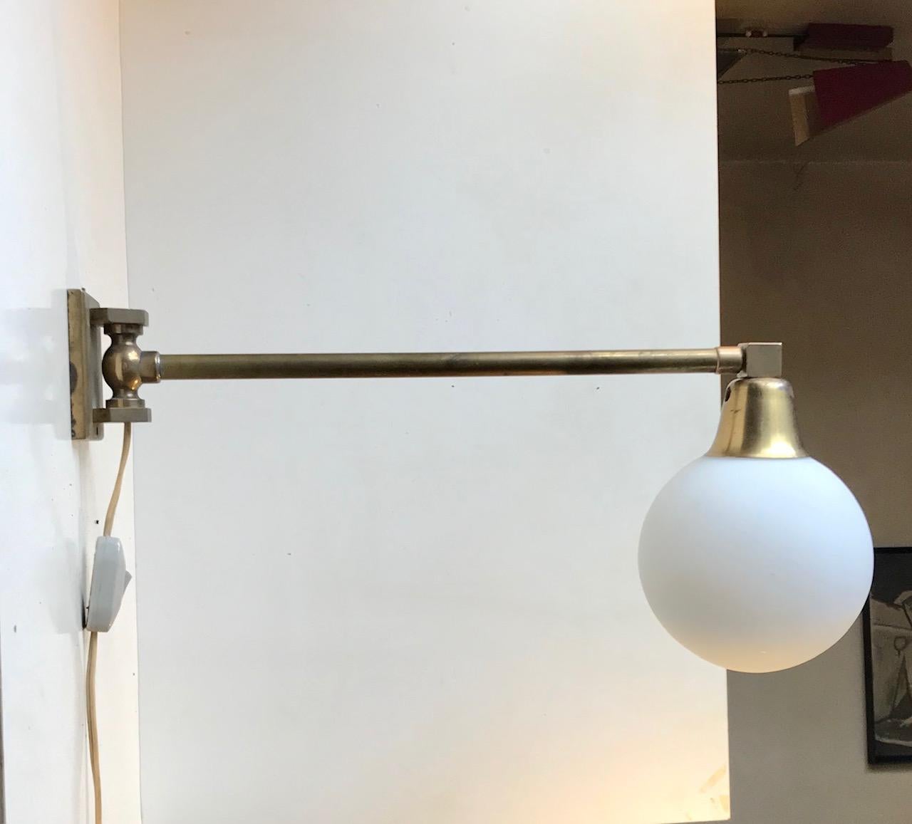 Side to side adjustable wall lamp composed of a solid heavy stock brass 'body' installed with a opaline ball shade. It was designed and manufactured in Scandinavia during the 1950s or 60s. The style is reminiscent of Svend Aage Holm-Sørensen and