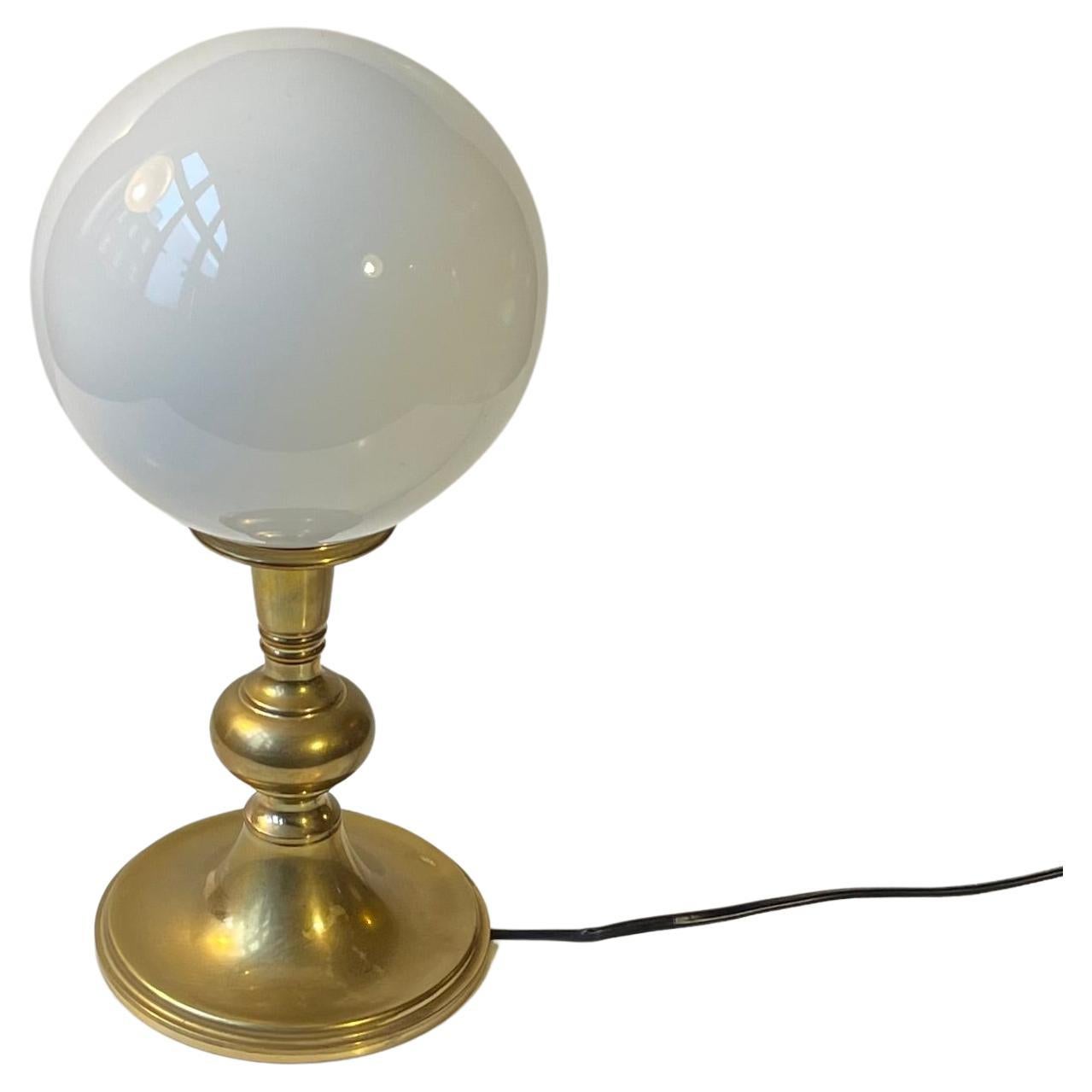 Simplistically composed Scandinavian Modern table Lamp. It features a heavy solid brass base and white opaline ball shade. It has an on/of switch to its cord. It was made in Sweden or Denmark during 1970s. The style of this light is Art Deco Revival