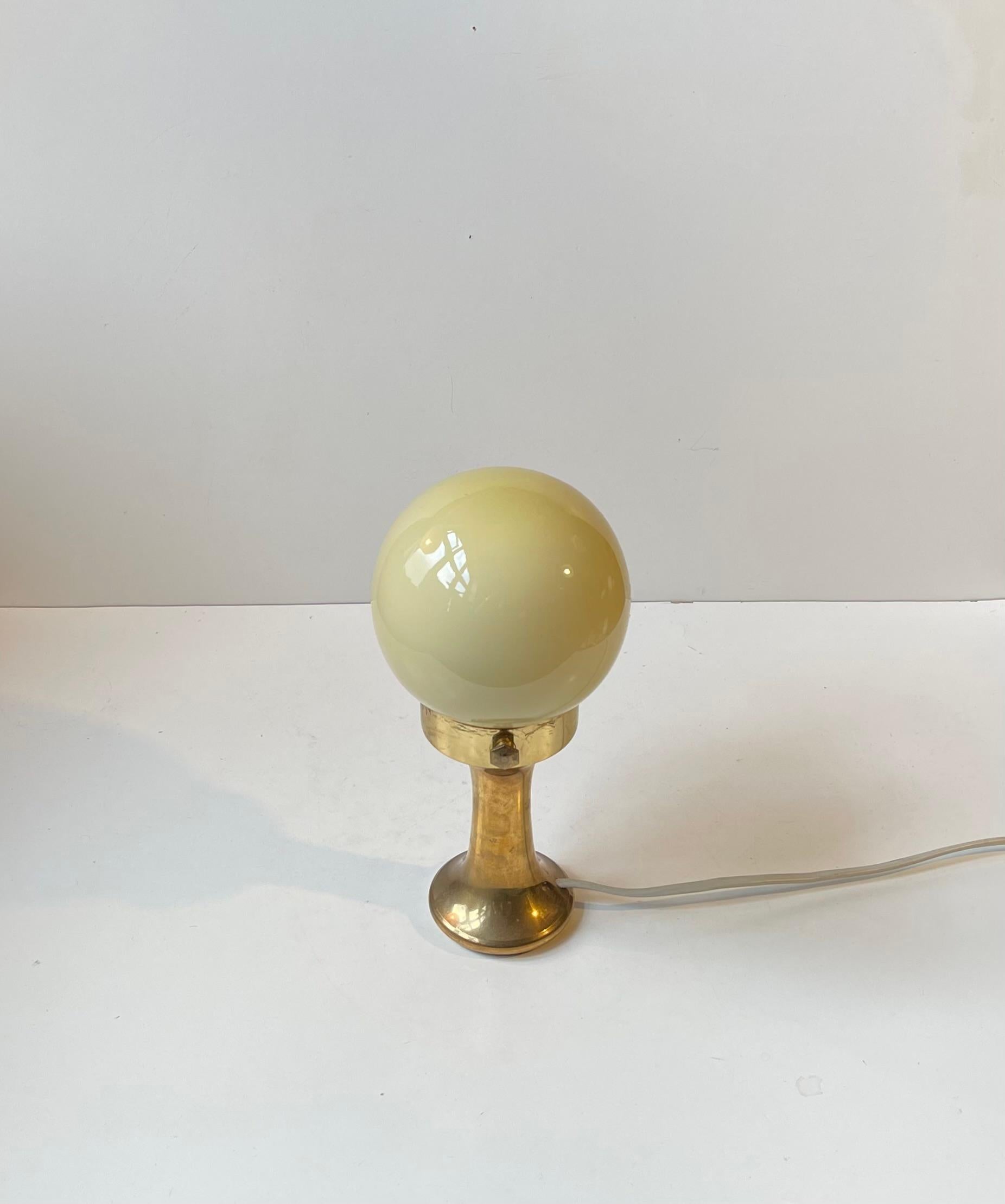 A small simplistically yet elegantly composed Table Lamp in solid brass and featuring a pastel yellow spherical shade. Made in Scandinavia during 1970s in art deco revival style. The style of this light resembles lights from Hans Agne Jakobsson and