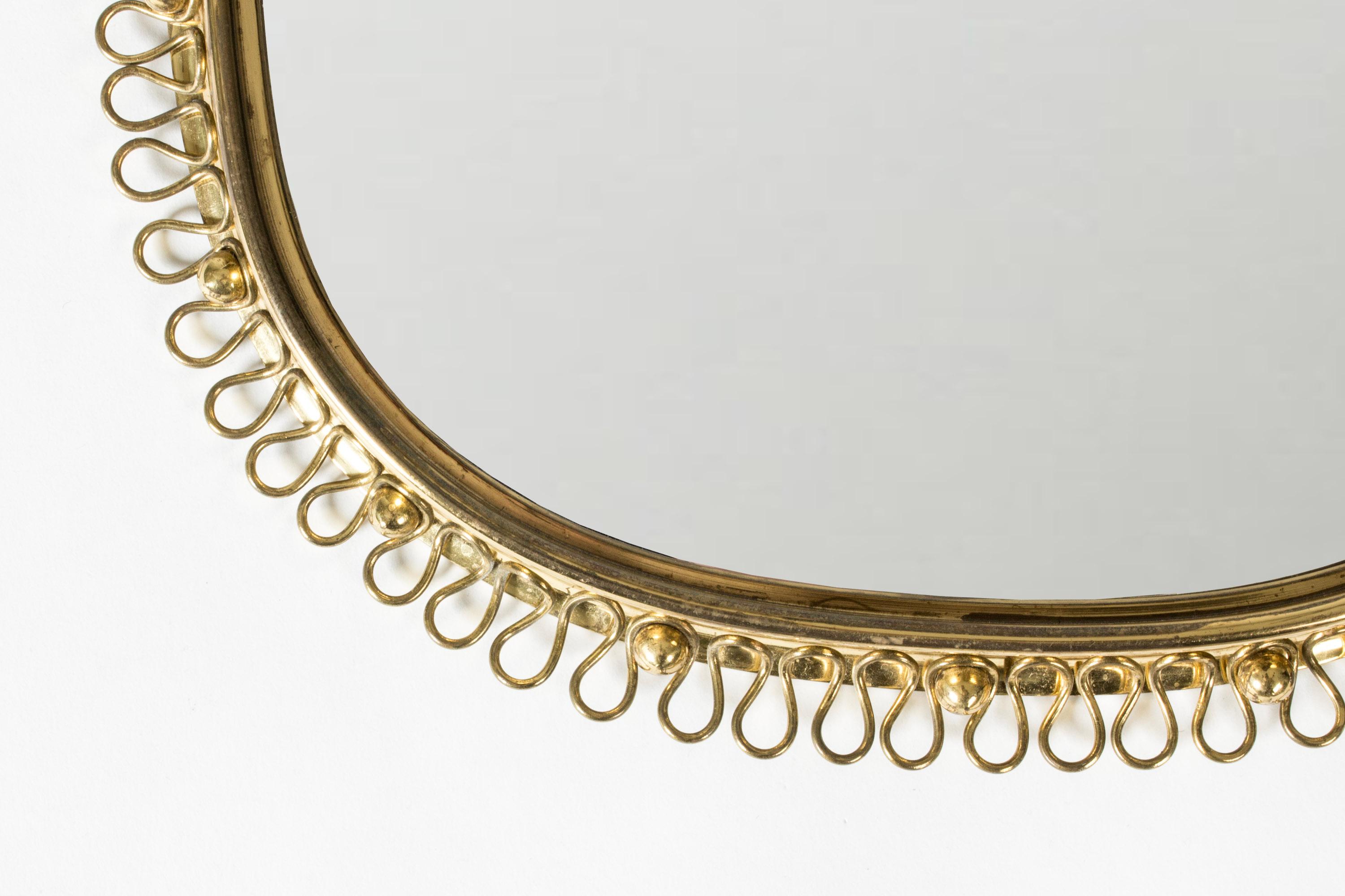 Beautiful Swedish Modern wall mirror, made from brass. Scalloped edge brass rim, decorative hoop for suspension.