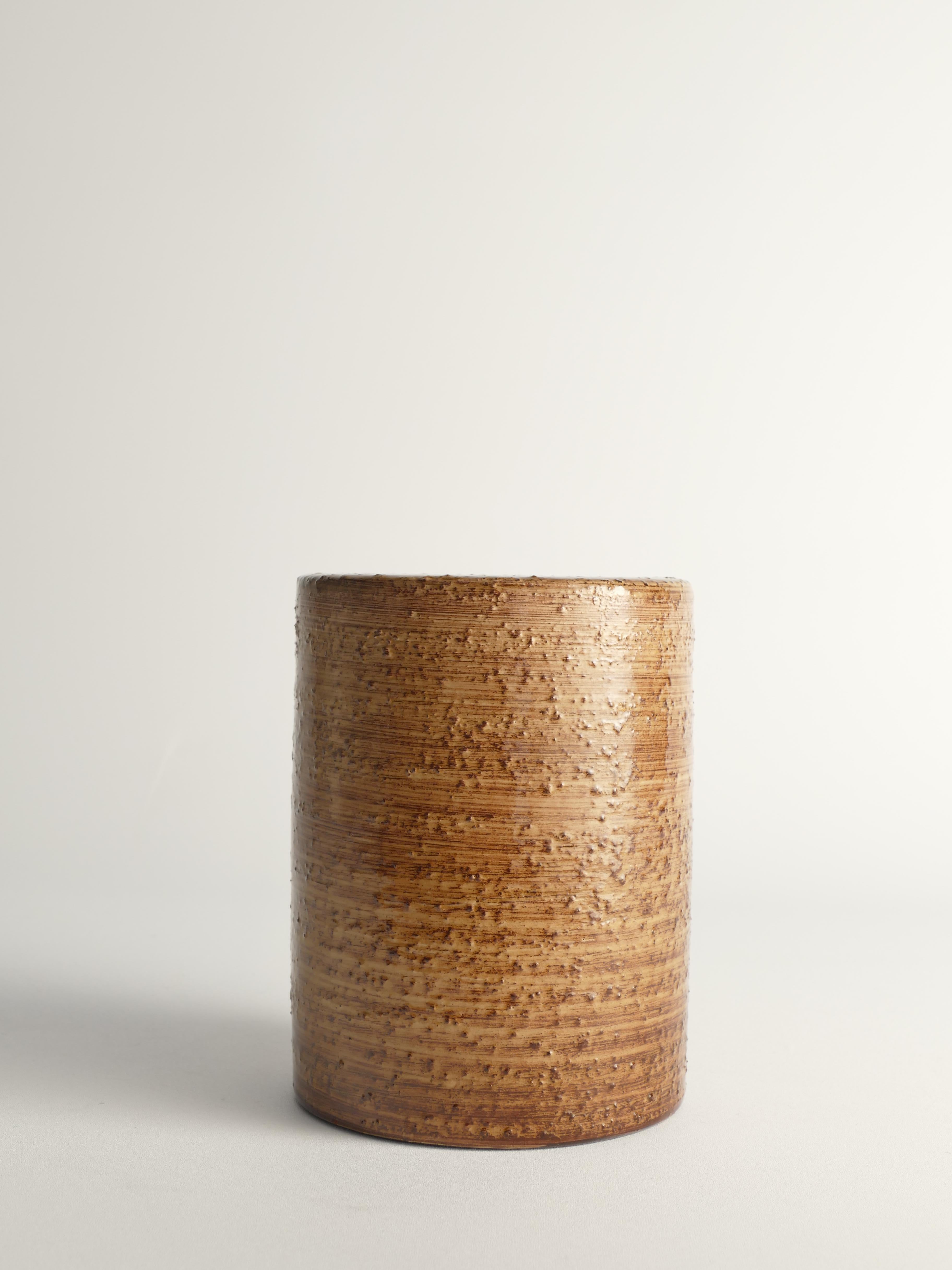 Questo robusto vaso di terracotta a forma di cilindro dell'artista Jerk Werkmäster è un pezzo notevole proveniente da Nittsjö, in Svezia. Realizzato in terracotta chamotte (grog), il vaso presenta uno smalto marrone senape scuro lucido e granuloso