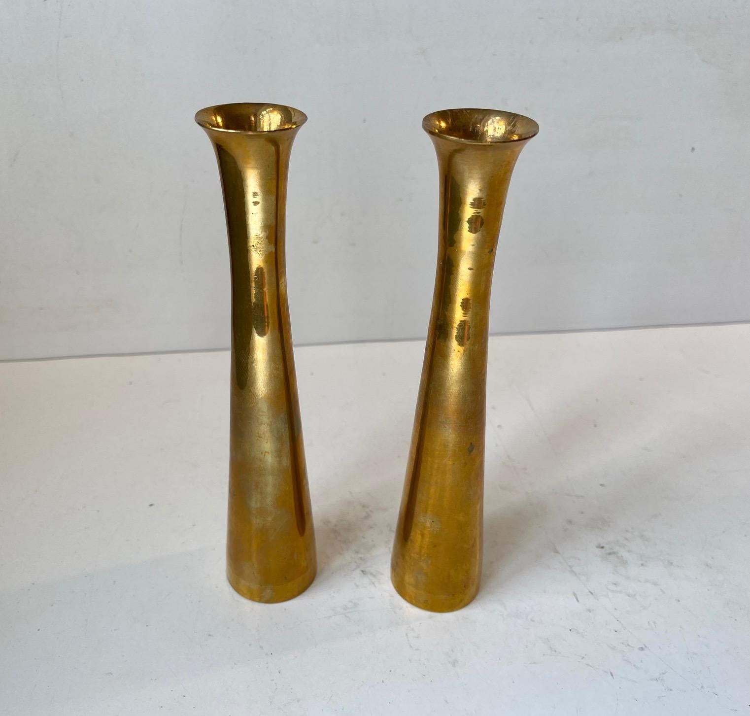 A pair of trumpet shaped brass candlesticks designed and manufactured in Scandinavia during the 1960s. The candlesticks are to be fitted with regular sixed candles. They have not been polished recently and display patina. The style of this set is