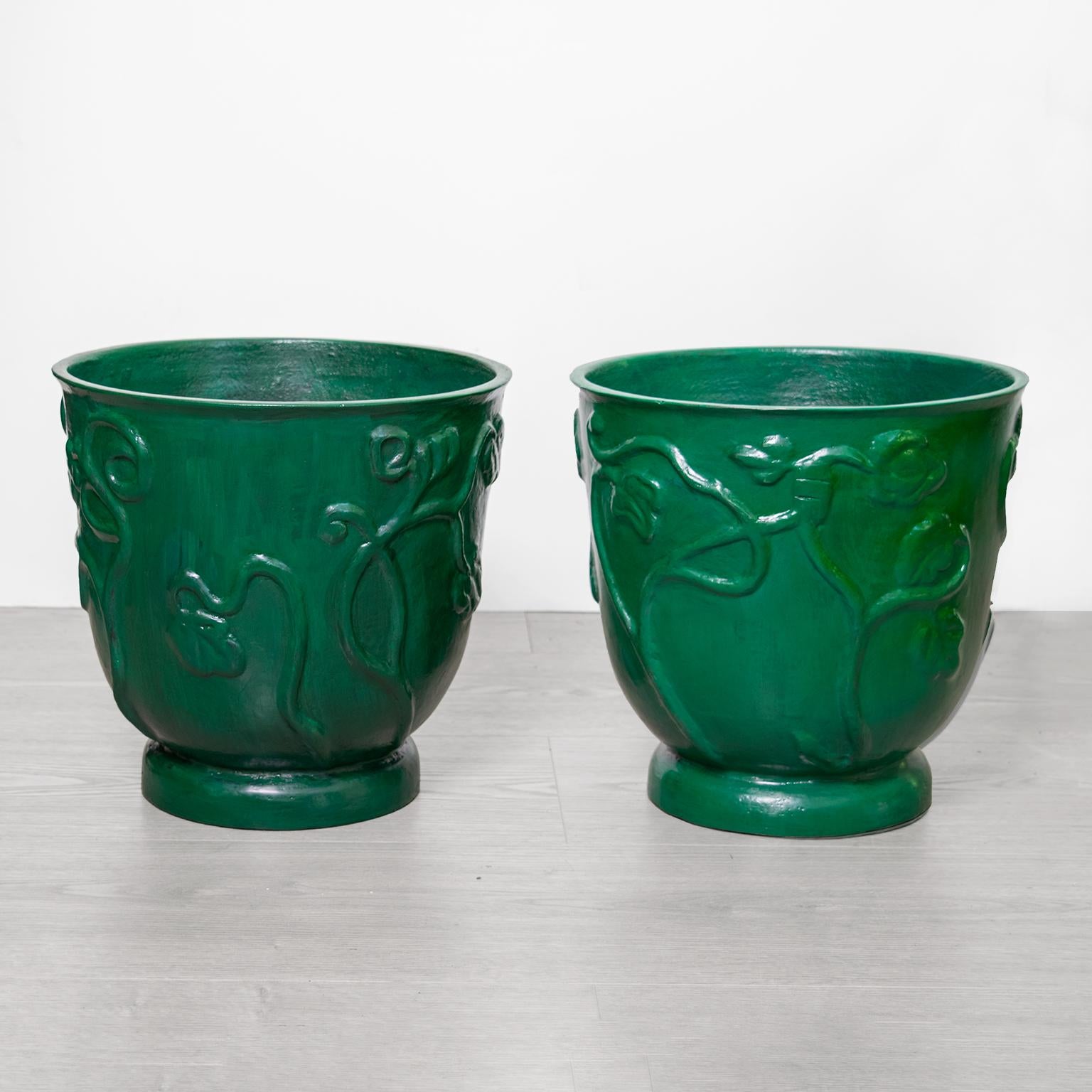 Pair of Scandinavian Modern, Carl Milles designed patinated cast iron urns. The urns have raised stylized floral designs and softly rounded bases. The urns have been newly patinated in deep greens. 

Carl Milles' work is internationally recognized