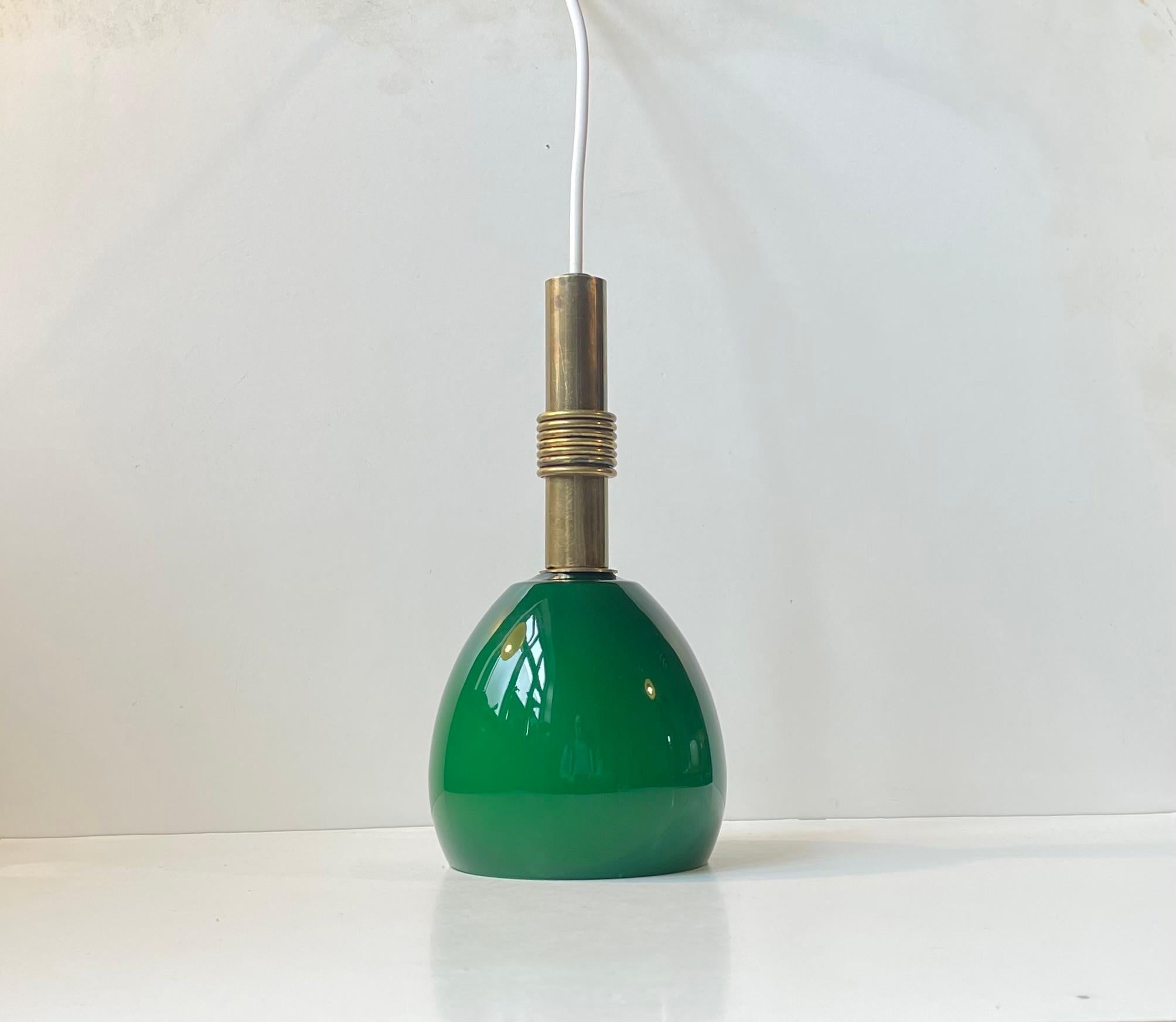 Un'elegante lampada a sospensione realizzata in ottone, con un anello decorativo in ottone e un paralume soffiato a mano in vetro opalino verde intenso. Sconosciuto designer scandinavo nello stile di Paavo Tynell, Vilhelm Lauritzen e Stilnovo.