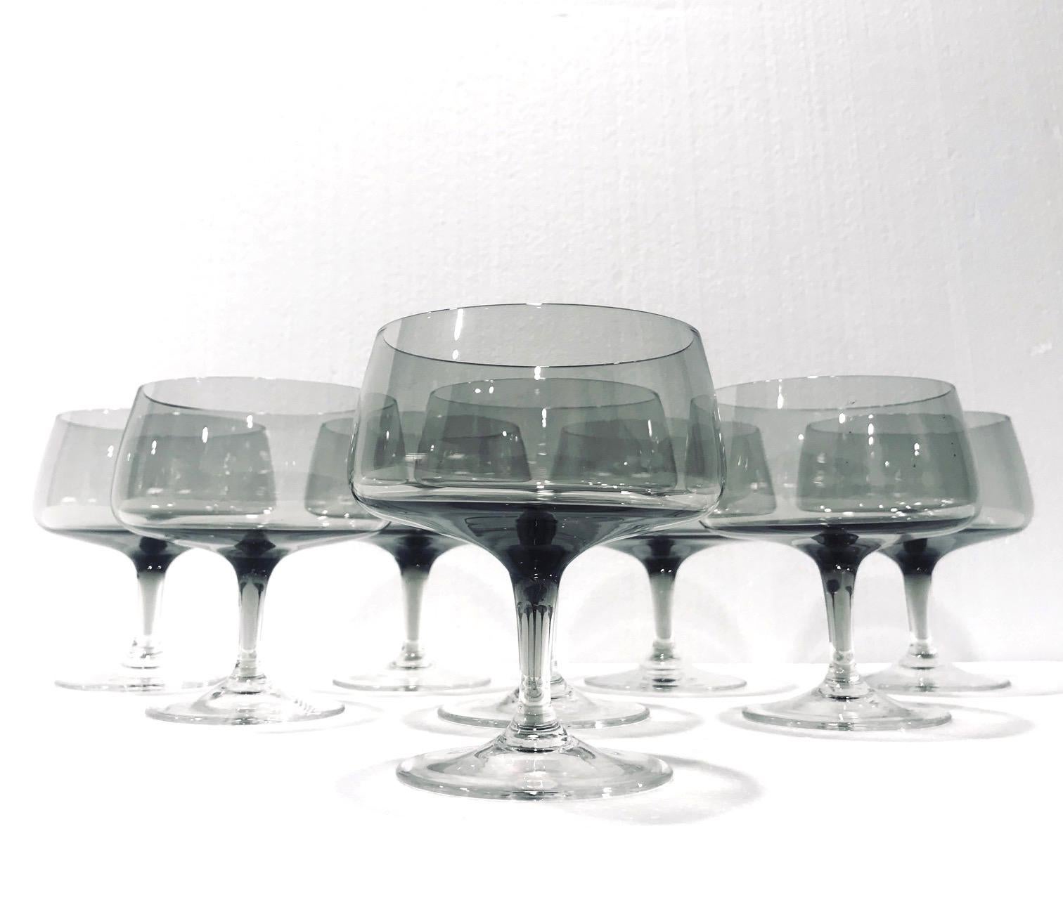 Set of seven Mid-Century Modern hand blown crystal champagne glasses in smoked grey. The glasses feature stylized bulbous saucer with narrow tapered stems and circular bases. This uber chic glasses make a beautiful addition to any barware or