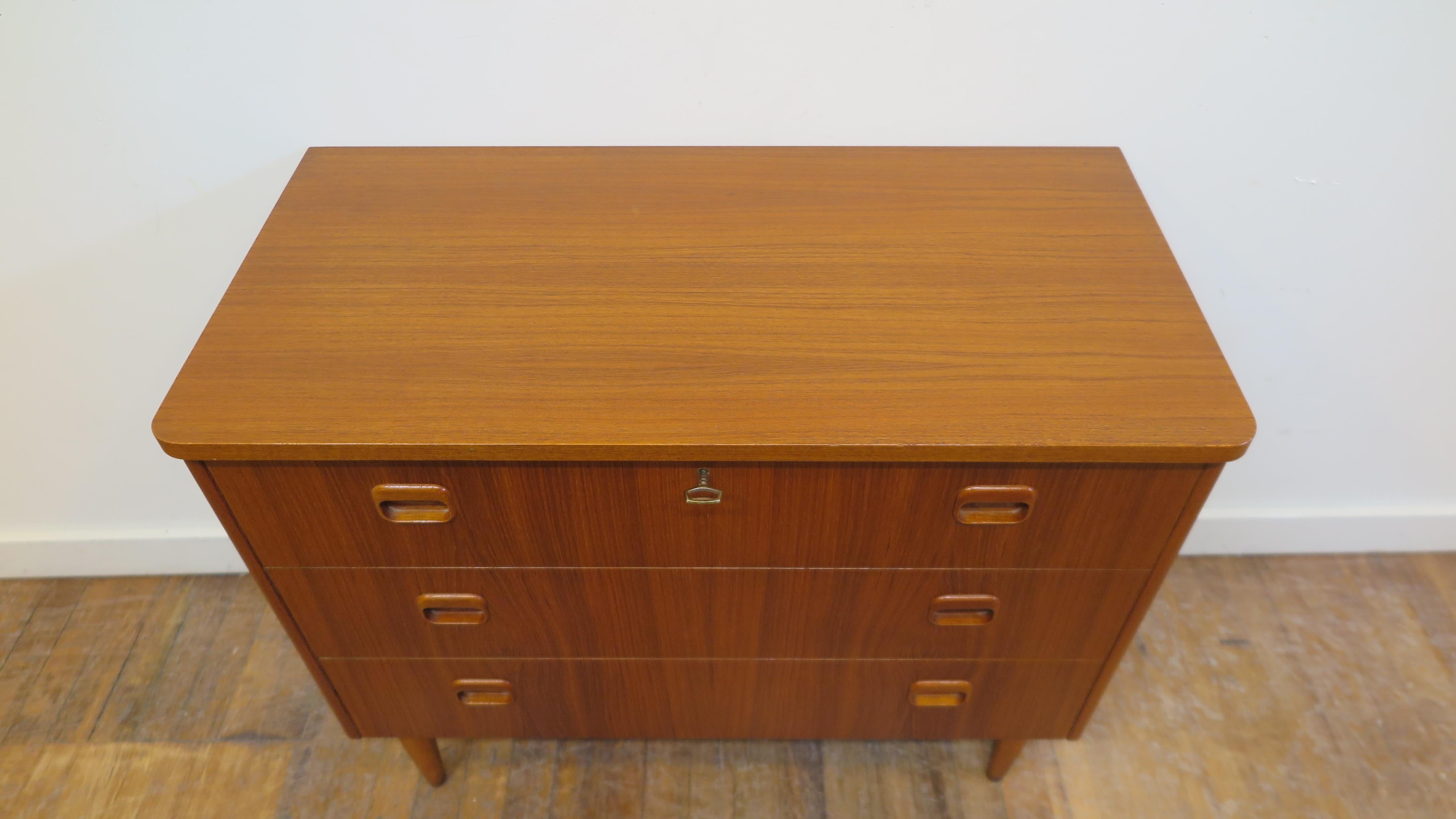 Scandinavian Modern mid century teak chest of drawers. Scandinavian Modern teak veneer chest of three drawers with top drawer lock and key, beach wood legs. Very good condition, clean inside and outside.