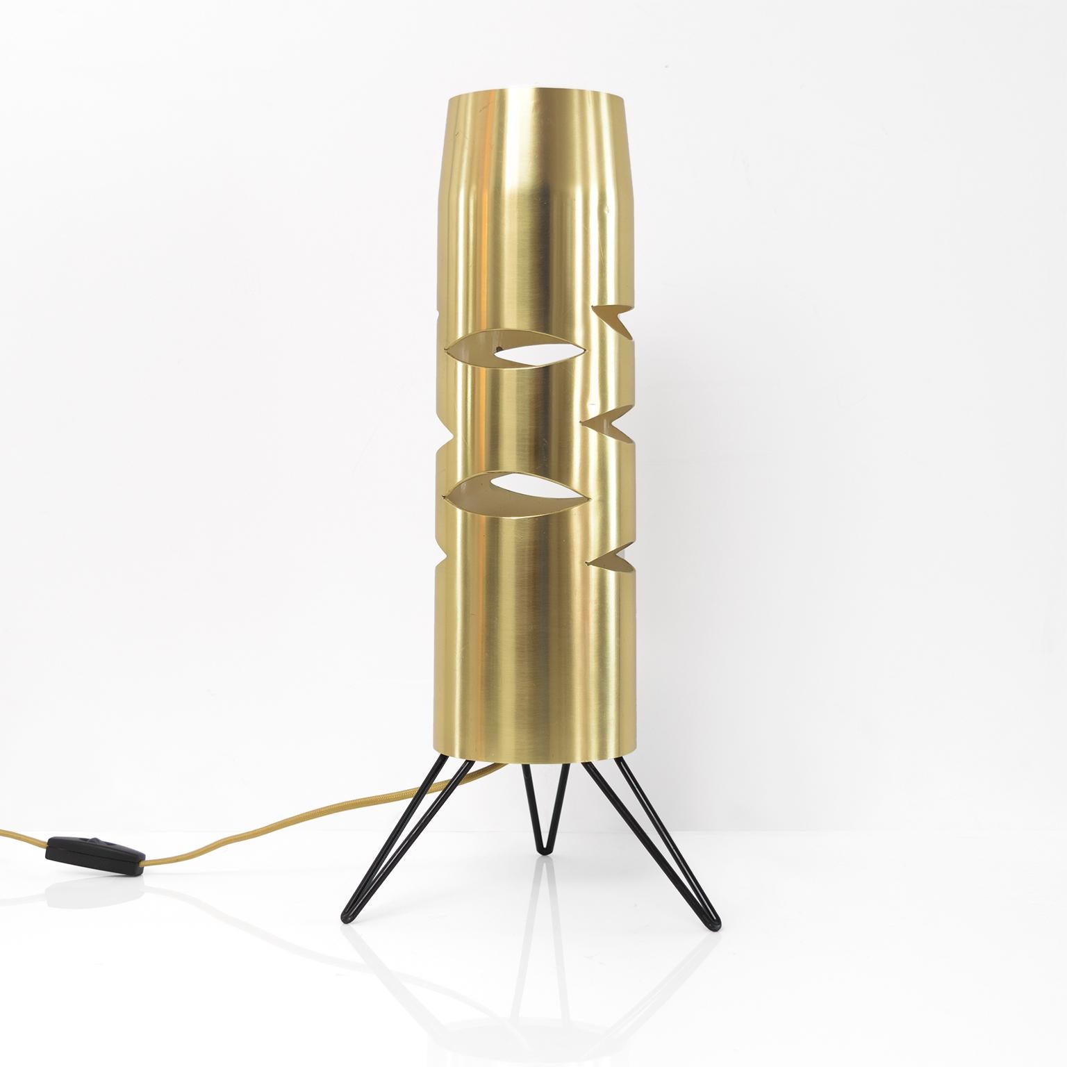 Scandinavian Modern polished solid brass cylindrical table lamp with eye shaped cutouts which references the surrealist movement. The lamps inside has it original baked enamel finish in an off white color. The tripod base is black lacquered metal,