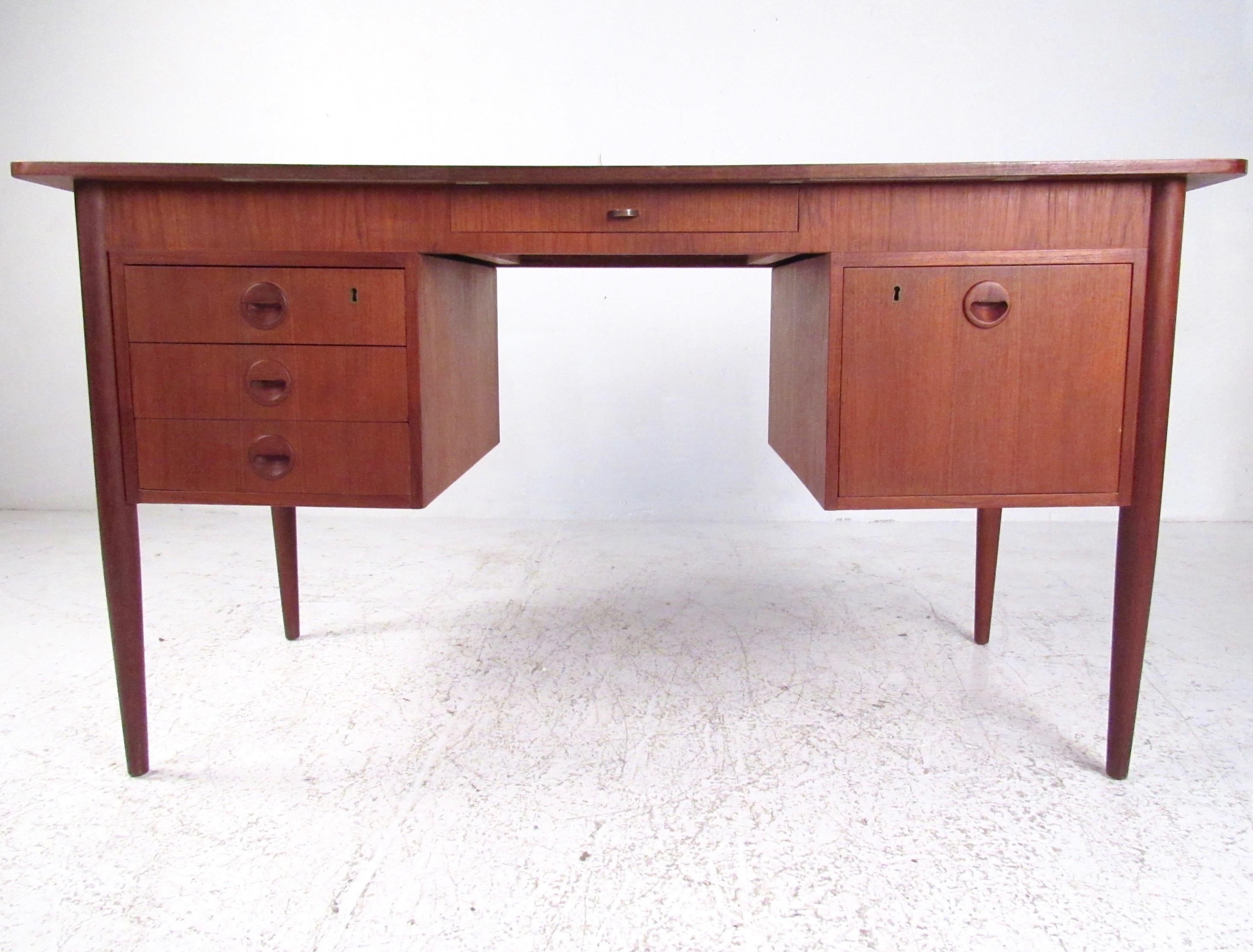 This striking Scandinavian Modern writing desk features Danish teak finish, sculptured drawer pulls, and quality vintage construction. This beautiful midcentury desk features double-sided finish and makes for an impressive addition to home or