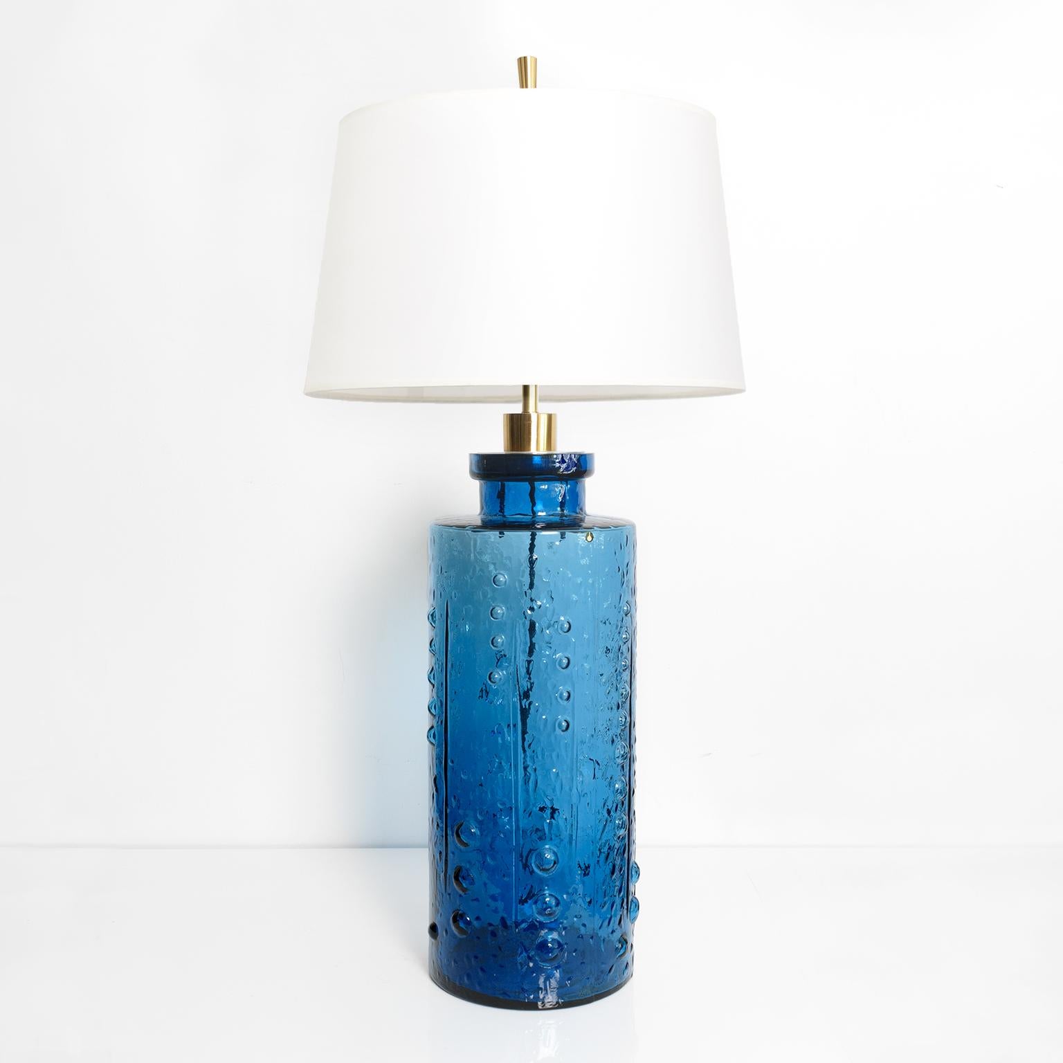 A tall deep blue Scandinavian Modern glass lamp by Pukeberg Glasbruk, Sweden, 1960’s. The cylindrical form has a textured surface of dots and vertical lines. The lamp has been new fitted with polished brass, custom hardware, stem and double cluster