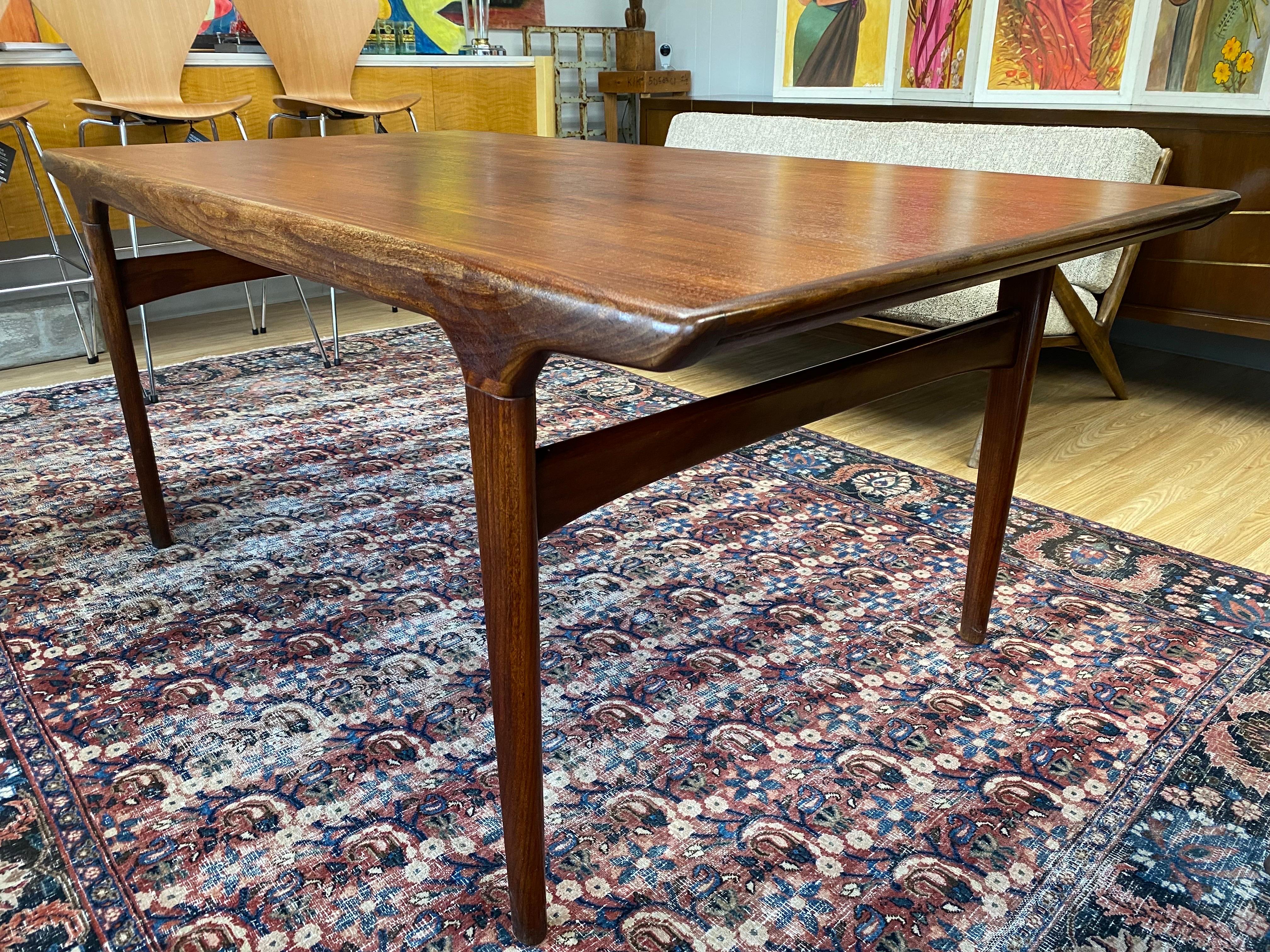 Danish modern teak dining table designed by Johannes Andersen, circa 1960s. This beautiful mid-century dining table features sculpted solid teak legs and a hidden extendable pull-out leaf underneath the table that can easily sit 8 people. This
