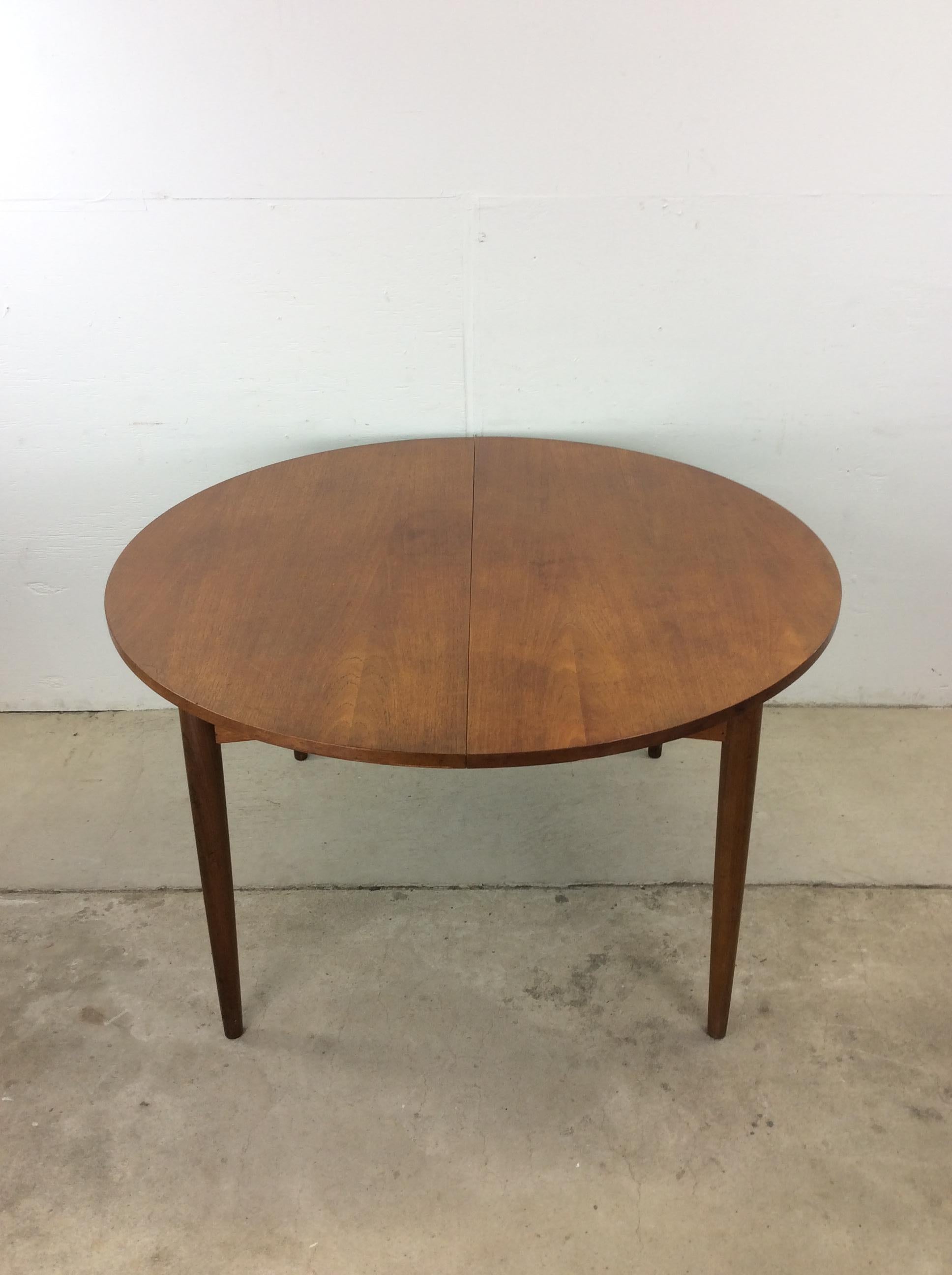 This Swedish modern dining table features hardwood construction, beautiful teak veneer with original finish, round design, one hide-a-way leaf with stored out of sight, and sitting on tall tapered legs.  Matching set of dining chairs available