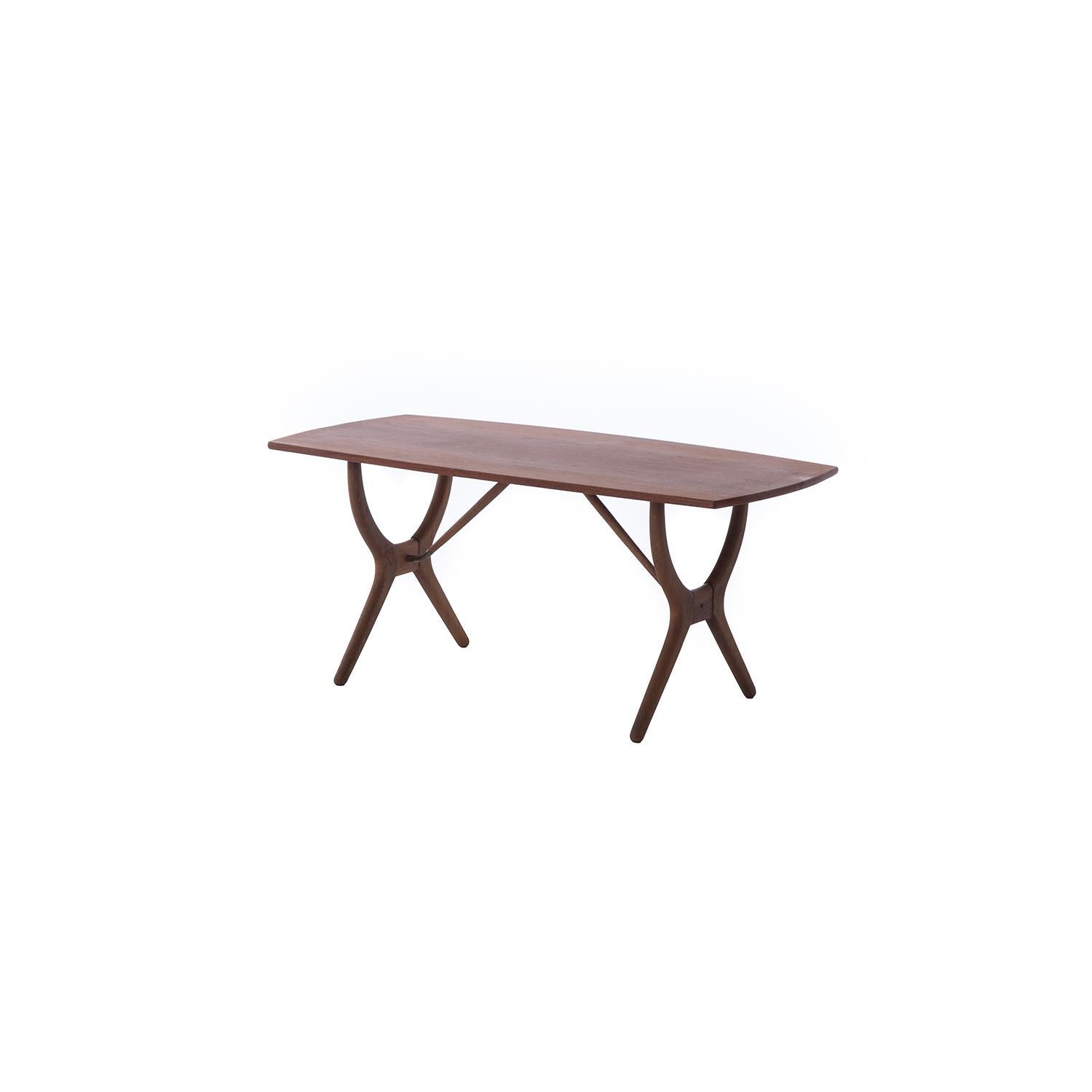 This Scandinavian modern teak coffee table has softly bowed edge details on the sides of the top and a complex wishbone shaped base with brass details. Made from old growth teak with an oil finish, this table has a beautiful patina. There is a light