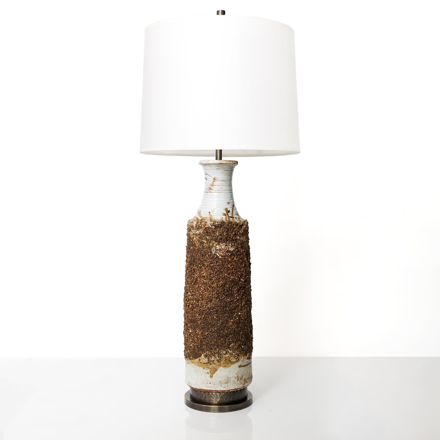 A tall hand thrown stoneware lamp by artist Eija Karivirta with hight textured surface over a white glaze. The lamp has custom hammered and patinated base and neck piece, a custom patinated brass double socket cluster, newly wired with standard