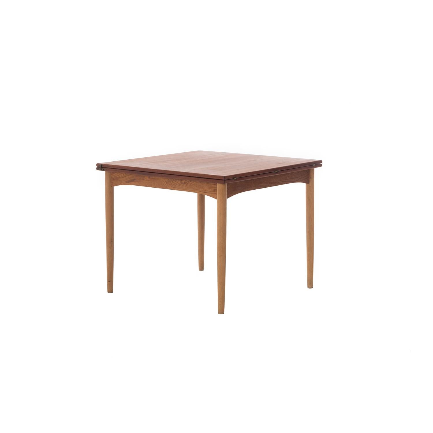 This elegant table opens from a square to a rectangle, the top slides over to accommodate the top. Apron is gently arched and lends to the table's sleek lines. Figured teak top with beautiful patina, brass hardware, oak skirt and legs. Børge