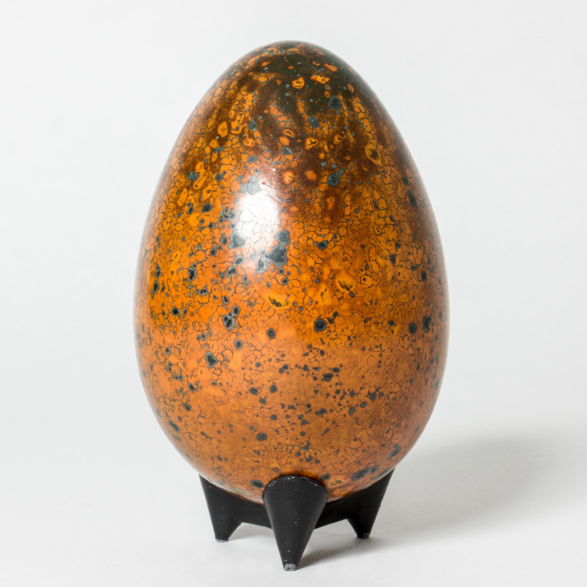 Beautiful egg formed sculpture by Hans Hedberg, made in faience. Intense orange colored glaze with lichen-like flecks giving an organic expression. Cast iron base.