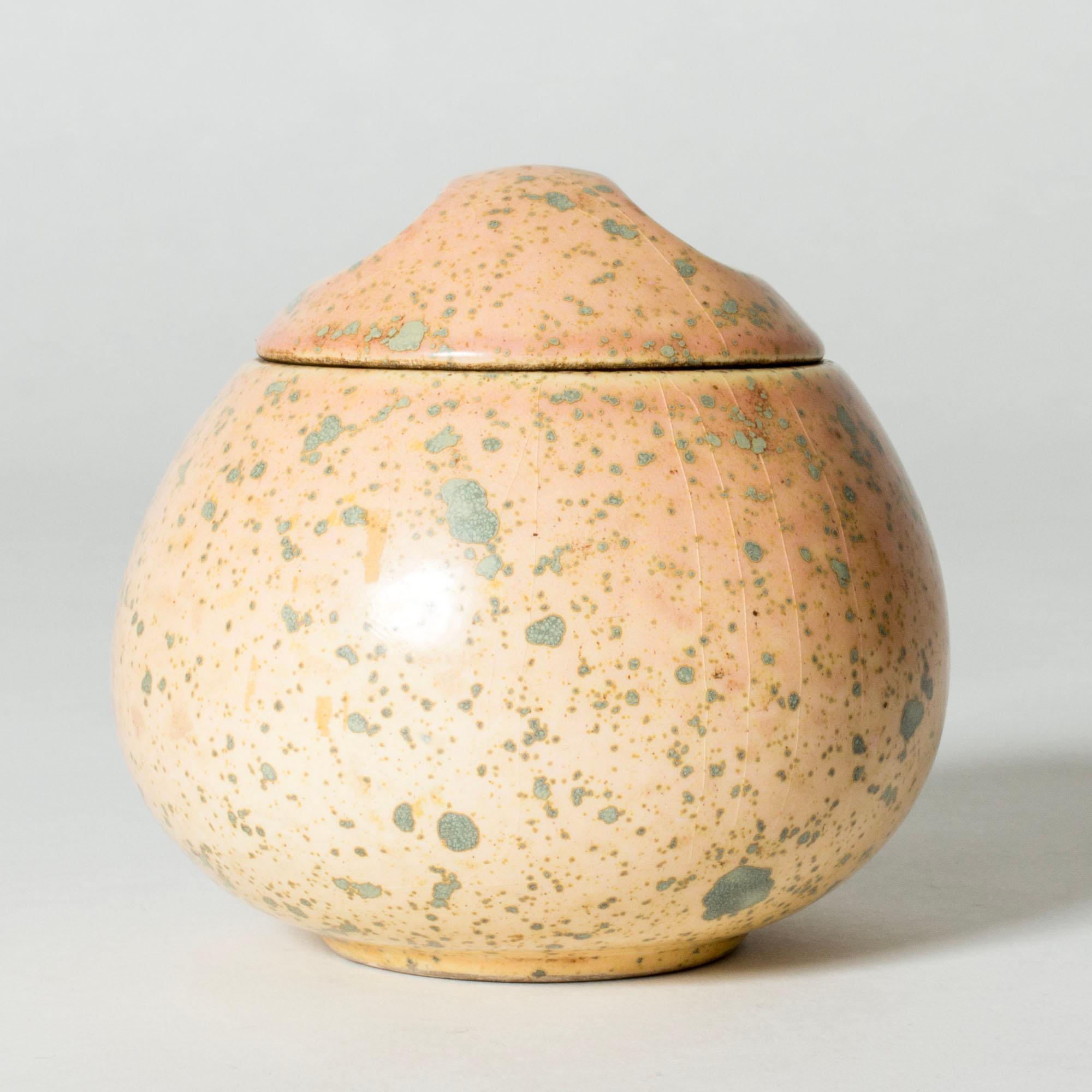 Grazioso vaso di Hans Hedberg, realizzato in maiolica di grande qualità. Forma grassa, a forma di uovo, con un coperchio con indici ovali. Smalto giallo pallido e rosato con macchie licheniche che conferiscono un'espressione organica.