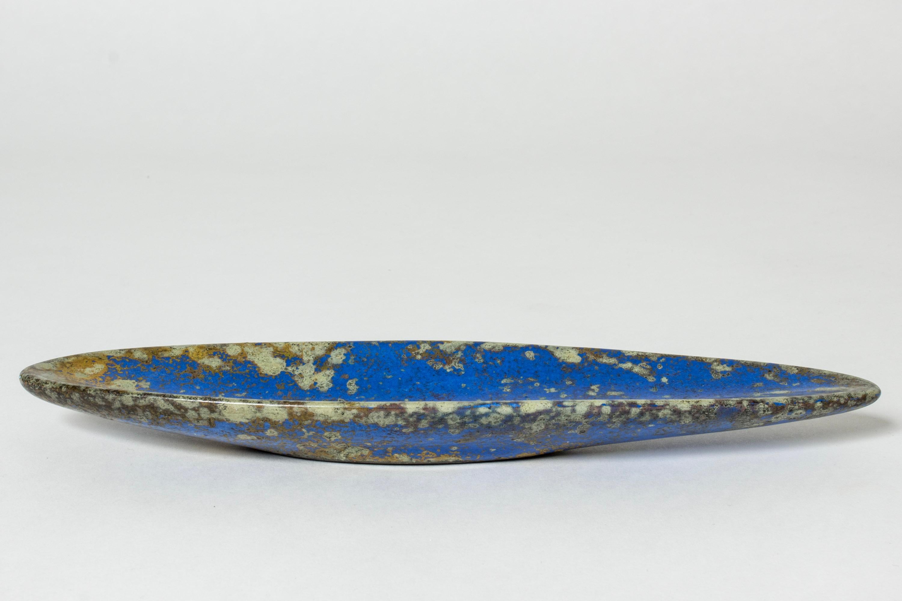 Beautiful small platter by Hans Hedberg, made in faience. Almond shaped with striking blue glaze covered with litchen-like flecks.