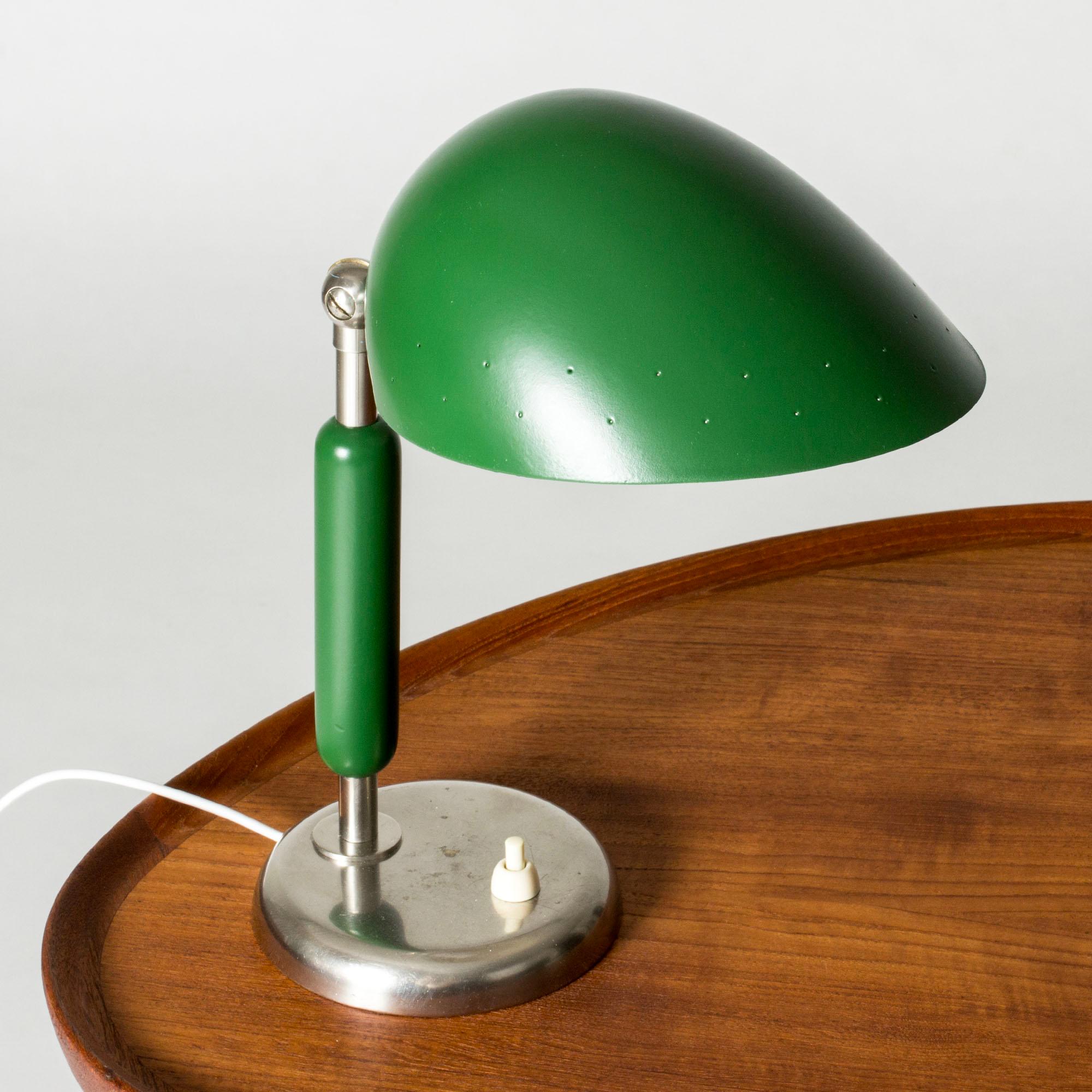 Adorable table or desk lamp by Harald Notini, with rounded, functionalist forms. White metal base, wooden handle lacquered green. Green lampshade with a pattern of small holes that let the light out when lit.