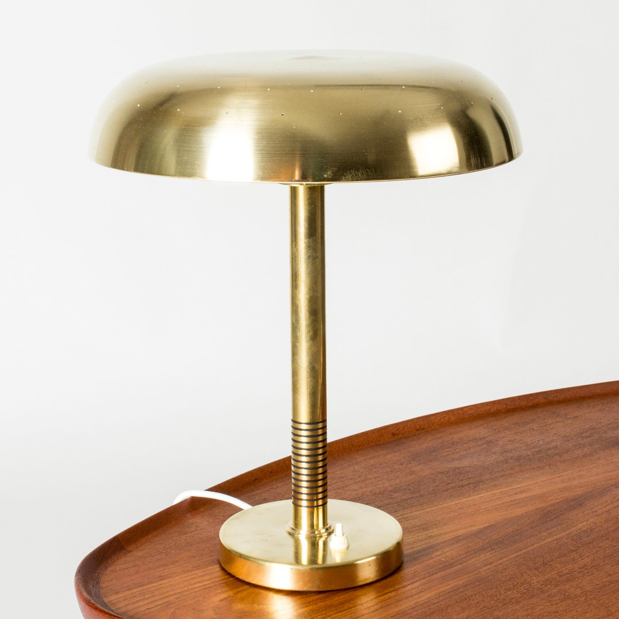 Lampe de table élégante de Boréns, en laiton. Large abat-jour en laiton aux formes arrondies, base avec d'élégantes rayures. Abat-jour perforé de petits trous qui laissent passer la lumière en douceur.