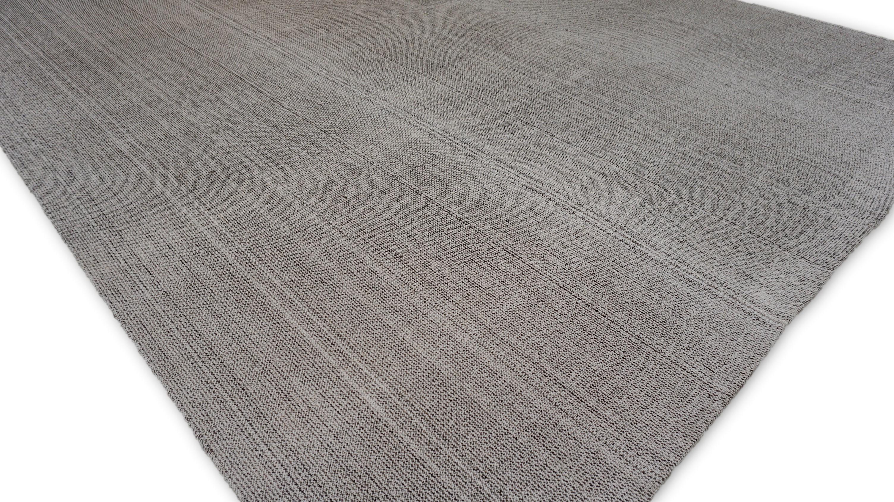 Questo tappeto in lana tessuto a mano presenta un elegante disegno a strisce lineari, tessuto in una morbida tavolozza di grigio, bianco e marrone con delicate variazioni tonali. Il motivo sobrio crea un senso di profondità e movimento, rendendolo