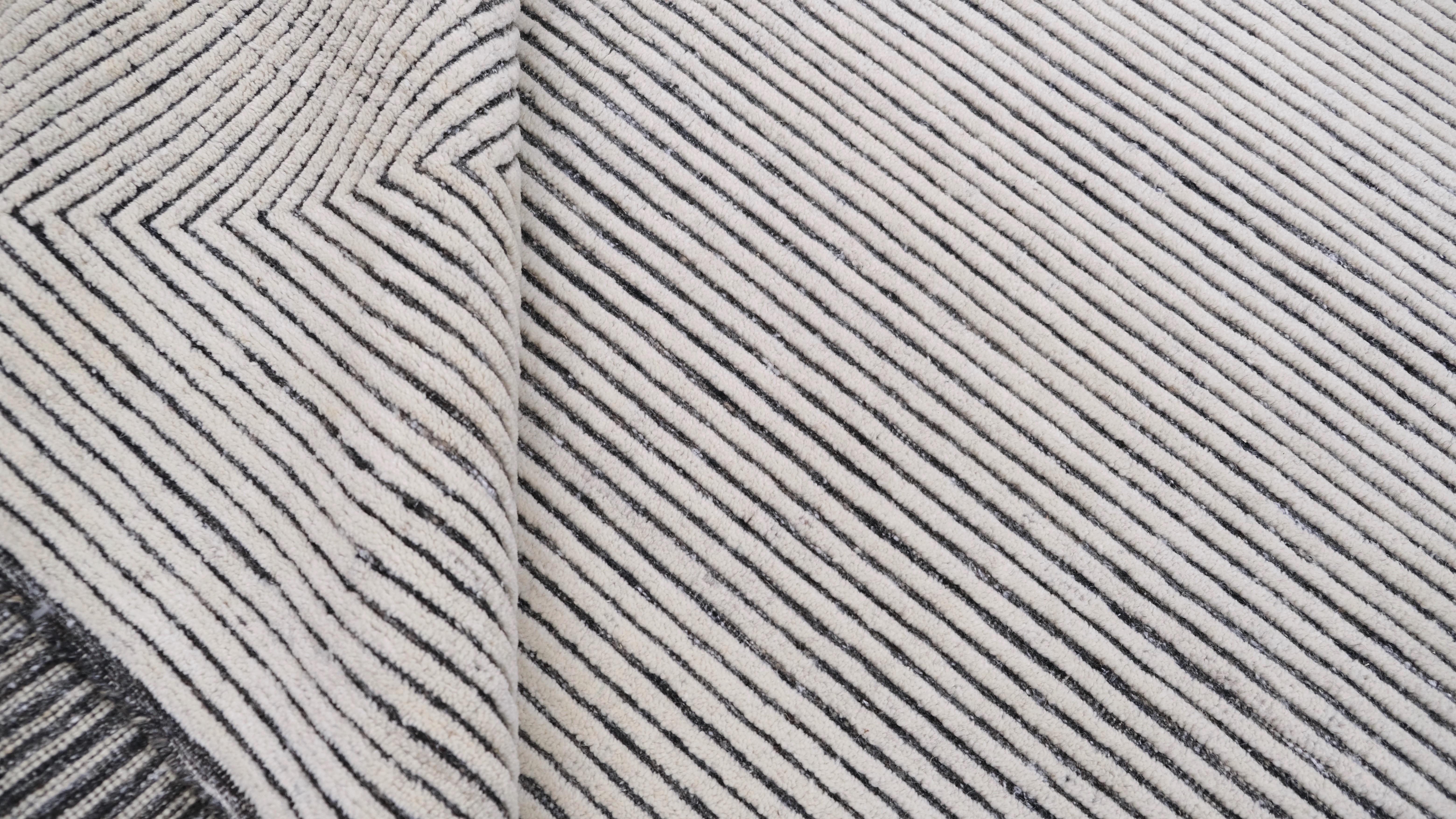 Tauchen Sie Ihren Raum in die moderne Eleganz dieses handgeknüpften Wollteppichs. Der Teppich weist ein auffälliges Muster mit konzentrischen elfenbeinfarbenen und grauen Linien auf, die zu einem kühnen geometrischen Motiv zusammenlaufen. Das