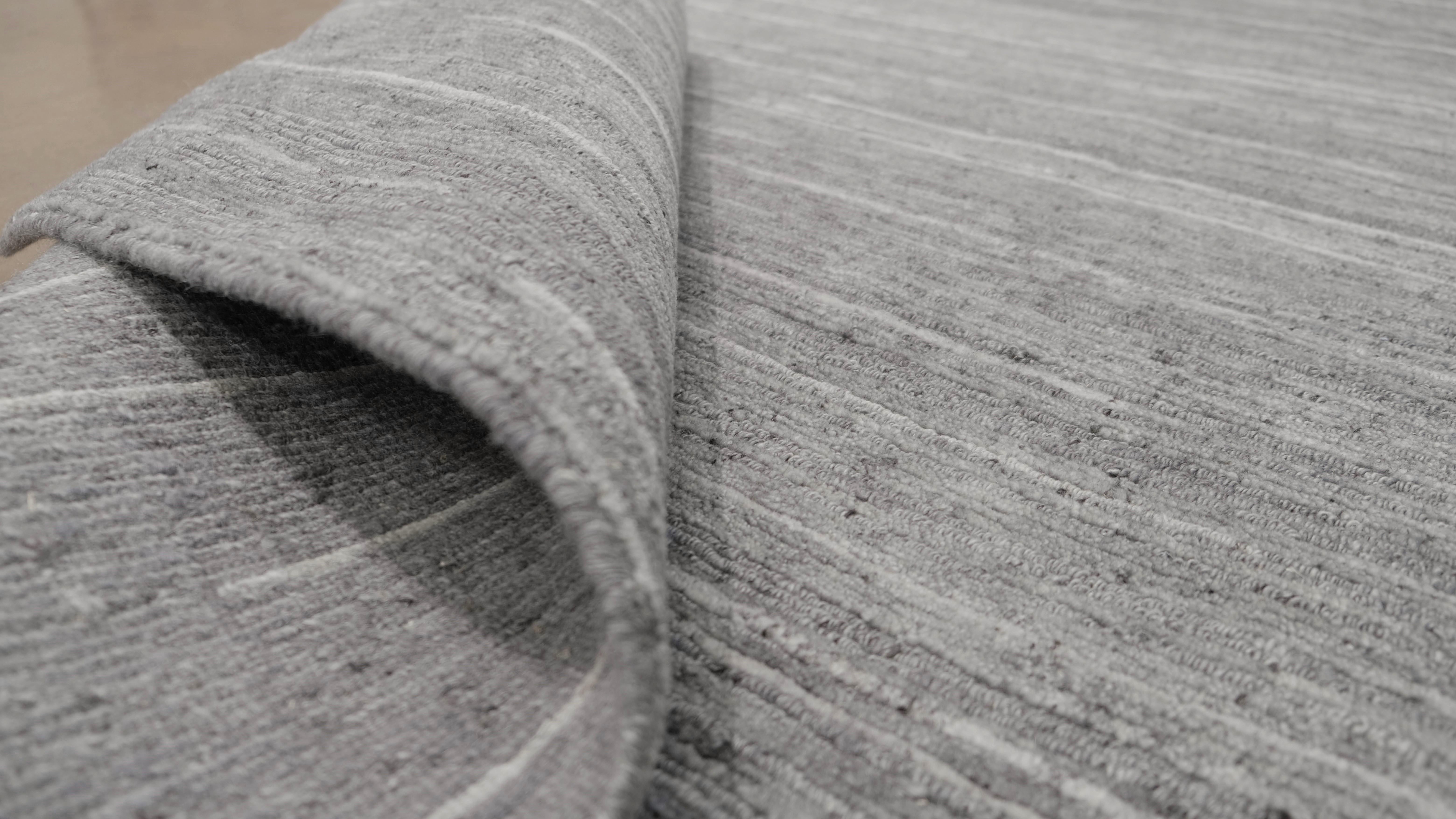 Verschönern Sie Ihr Zuhause mit diesem exquisiten handgeknüpften Wollteppich. Dieser Teppich mit seinem raffinierten, minimalistischen Design ist mit zarten, linearen Streifen in dezenten Grautönen verziert, die eine ruhige und anspruchsvolle