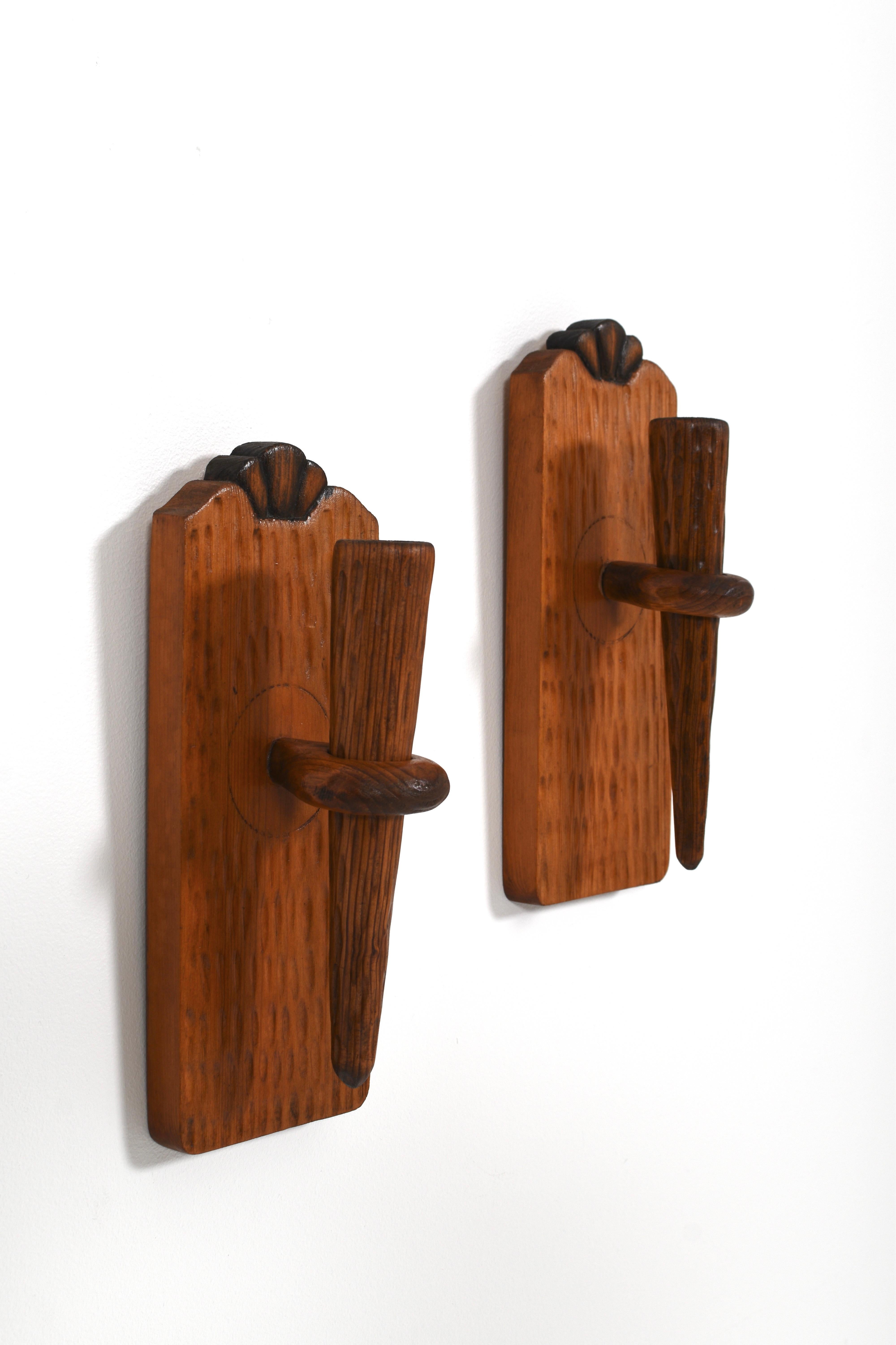 Beautifully handcrafted in Sweden during the 1940s, this pair of Scandinavian Modern wall-mounted candle holders showcases the warmth and character of solid pine. With sculptural lines, soft curves and carved shell-like details at the top, the